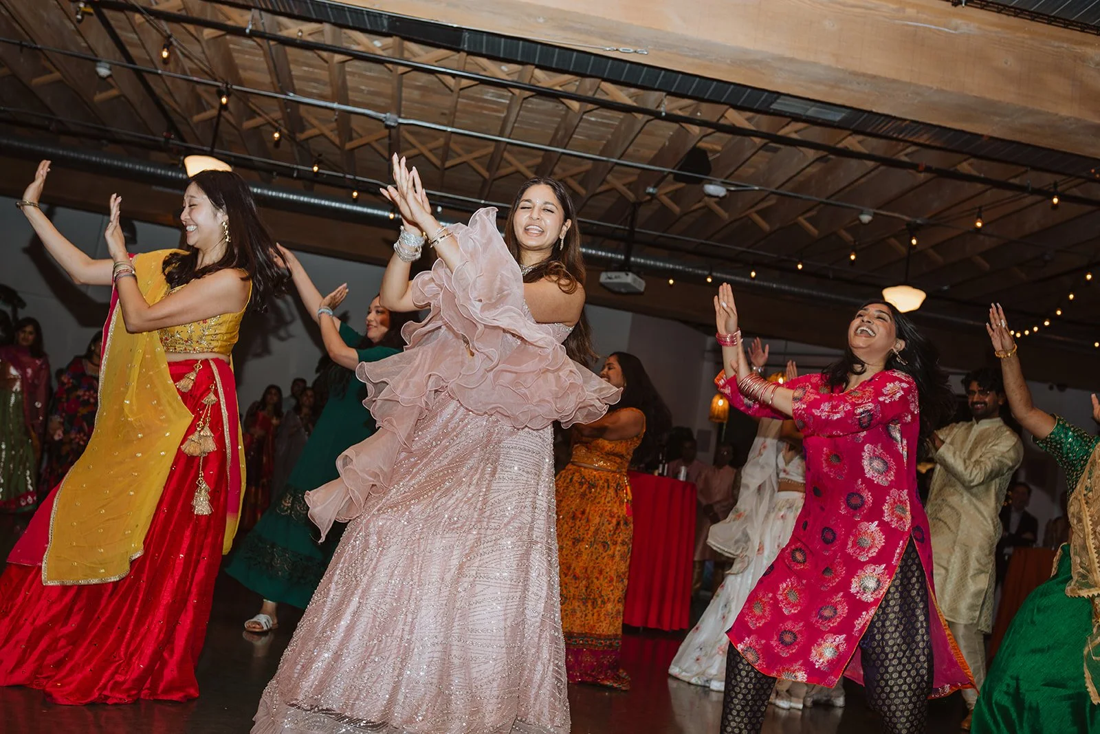 People dancing and celebrating at an indoor event, wearing colorful traditional attire.