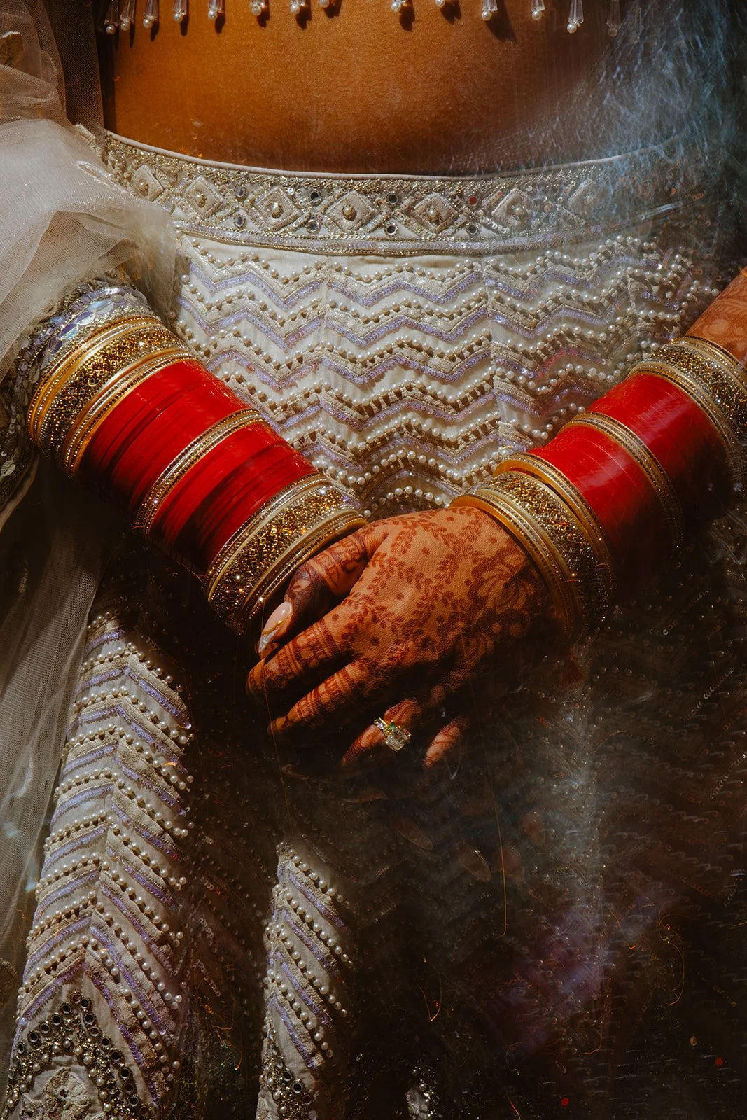 Close-up of an Indian bride's hands and arms adorned with traditional Indian jewelry and bangles, wearing ornate embroidered lehenga and henna designs.
