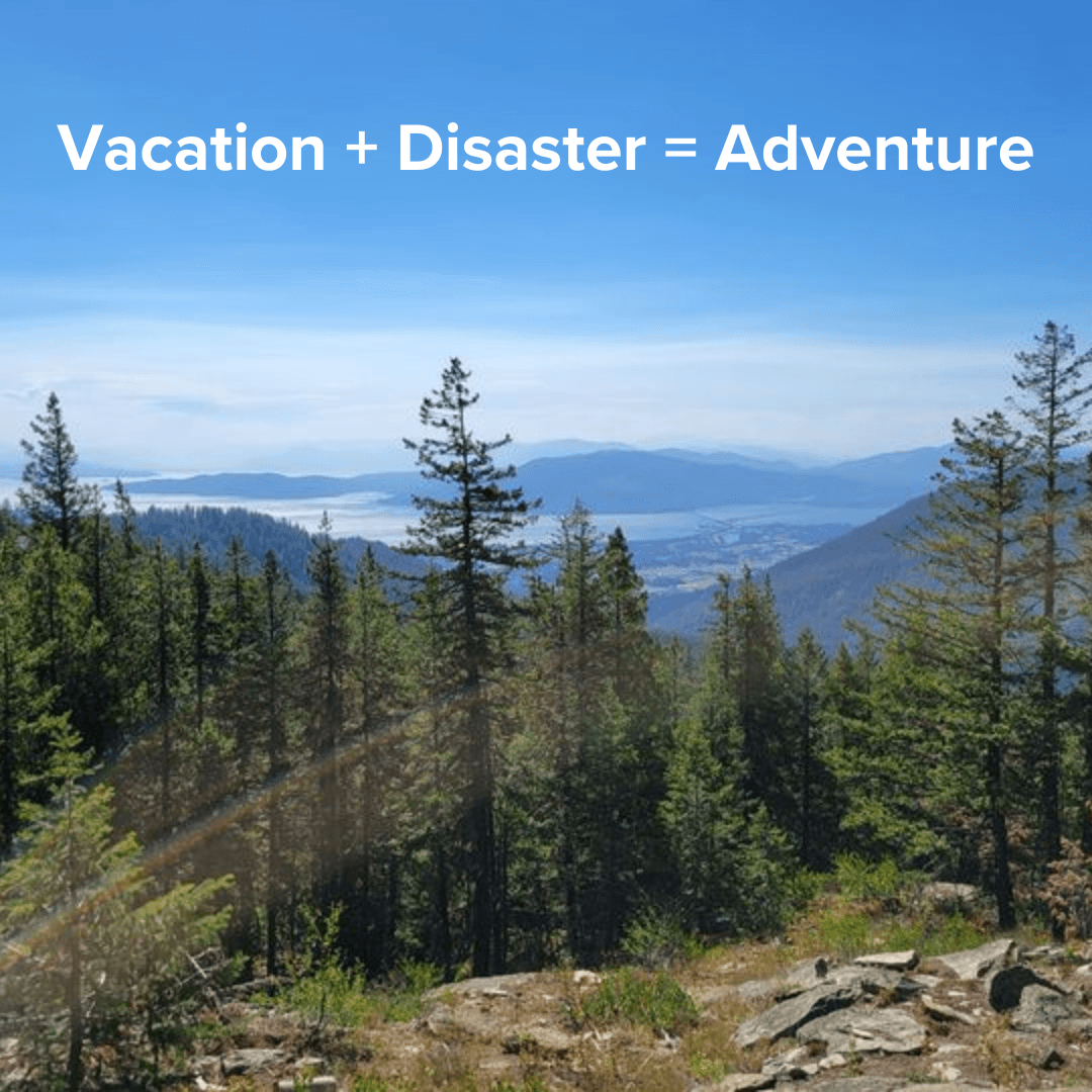 Title: "Vacation + Disaster = Adventure" in white on top. It's a photo of the top of a mountain forest with a lake below. A brown smudge is present across the bottom of the image.