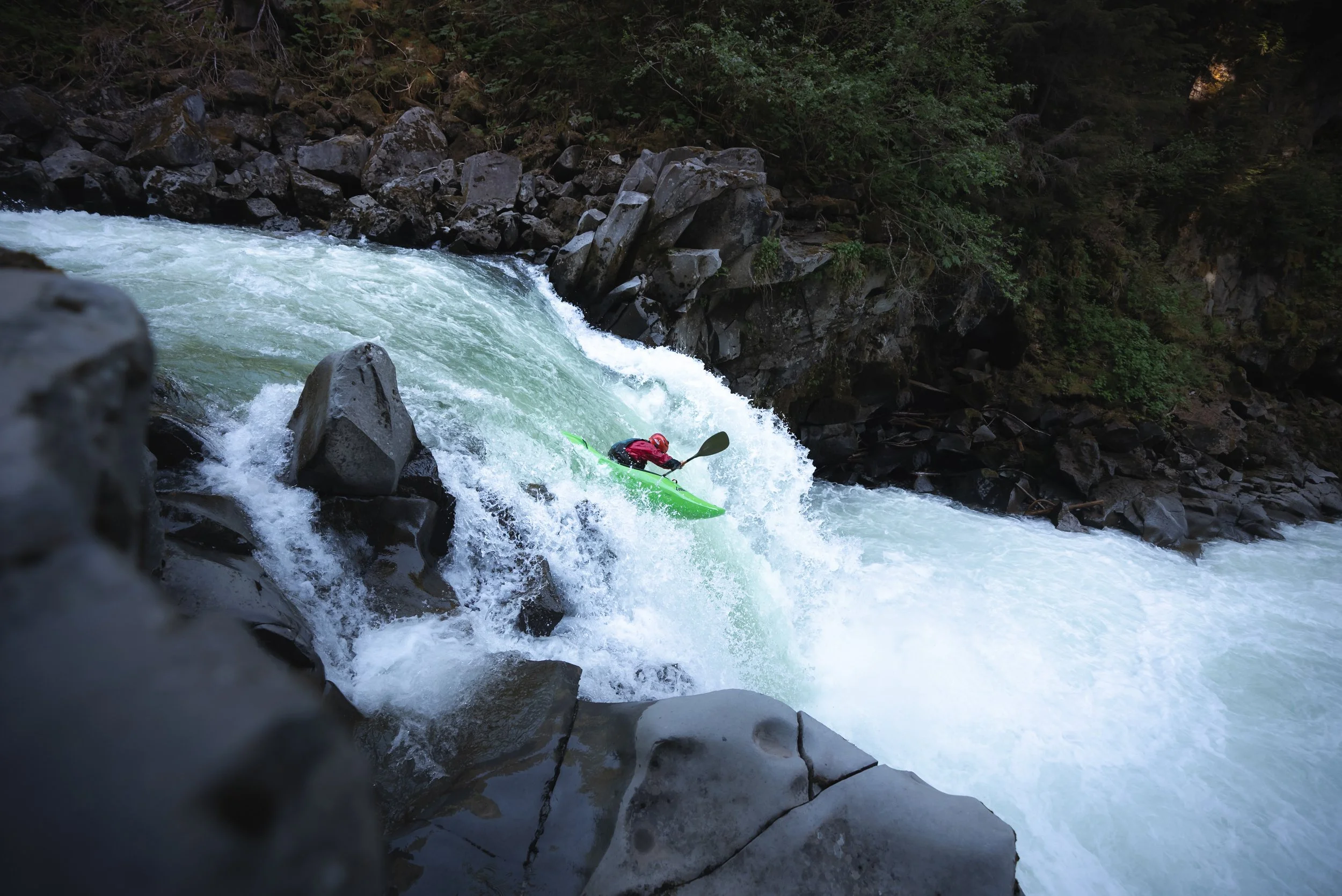 A person kayaking down a rapid river surrounded by rocks and dense forest.