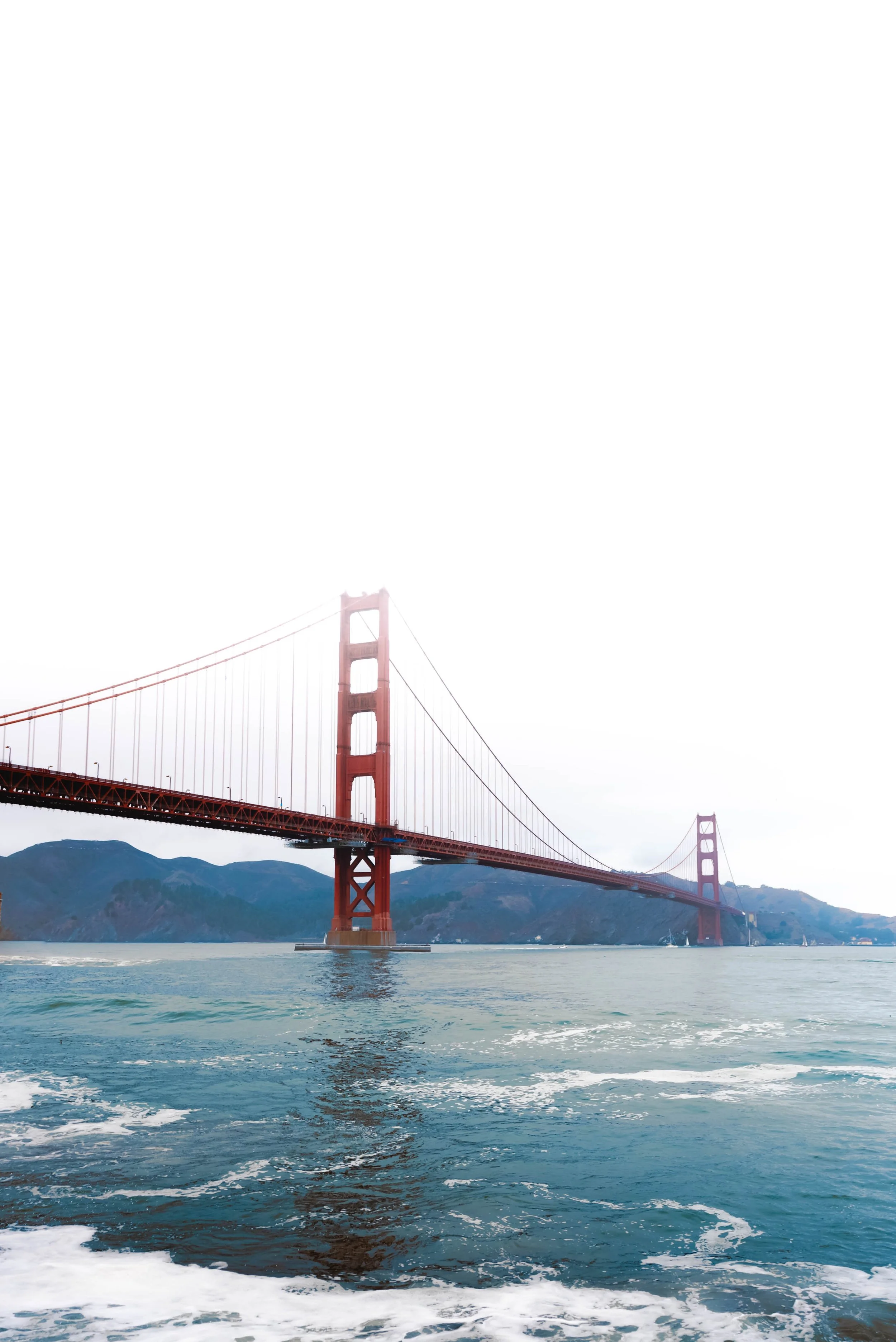 The Golden Gate Bridge in San Francisco, California, partially shrouded in fog with water and mountains in the background.