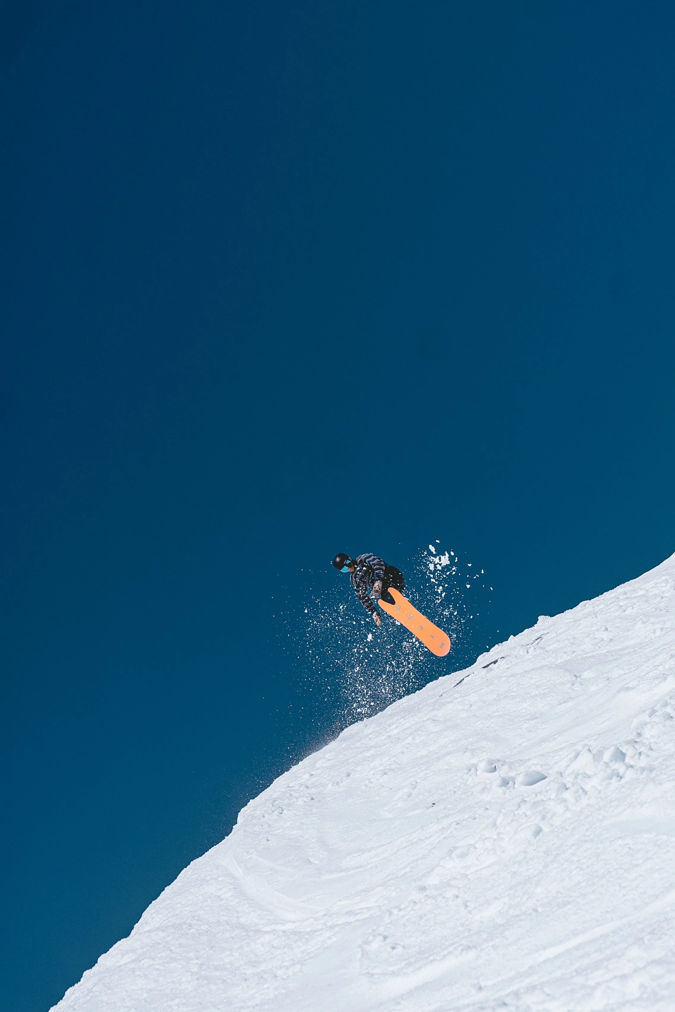 A skier in a striped jacket and helmet jump off a snowy slope against a clear blue sky.