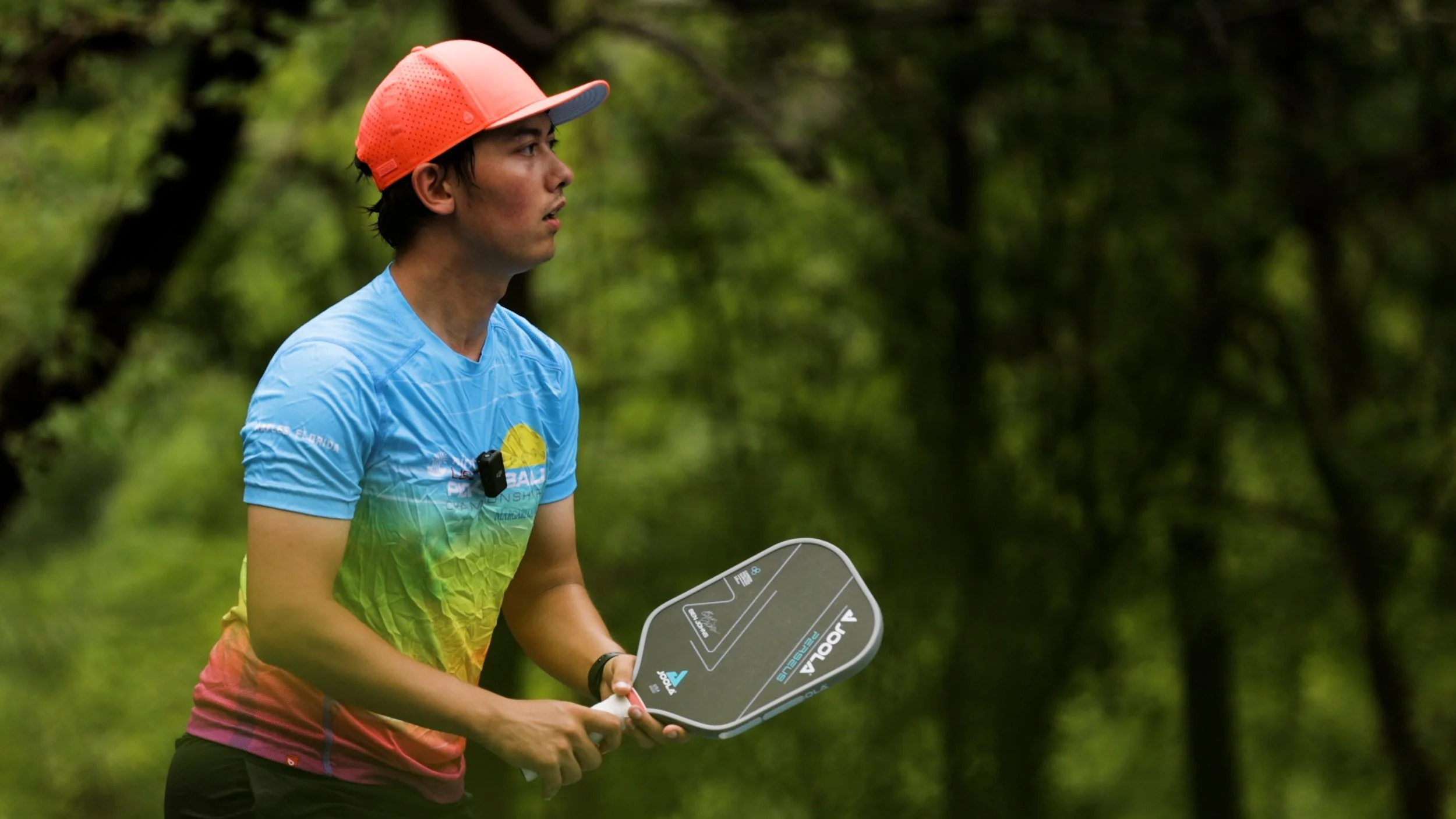 Player in a colorful shirt ready position holding a JOOLA Ben Johns Perseus pickleball paddle