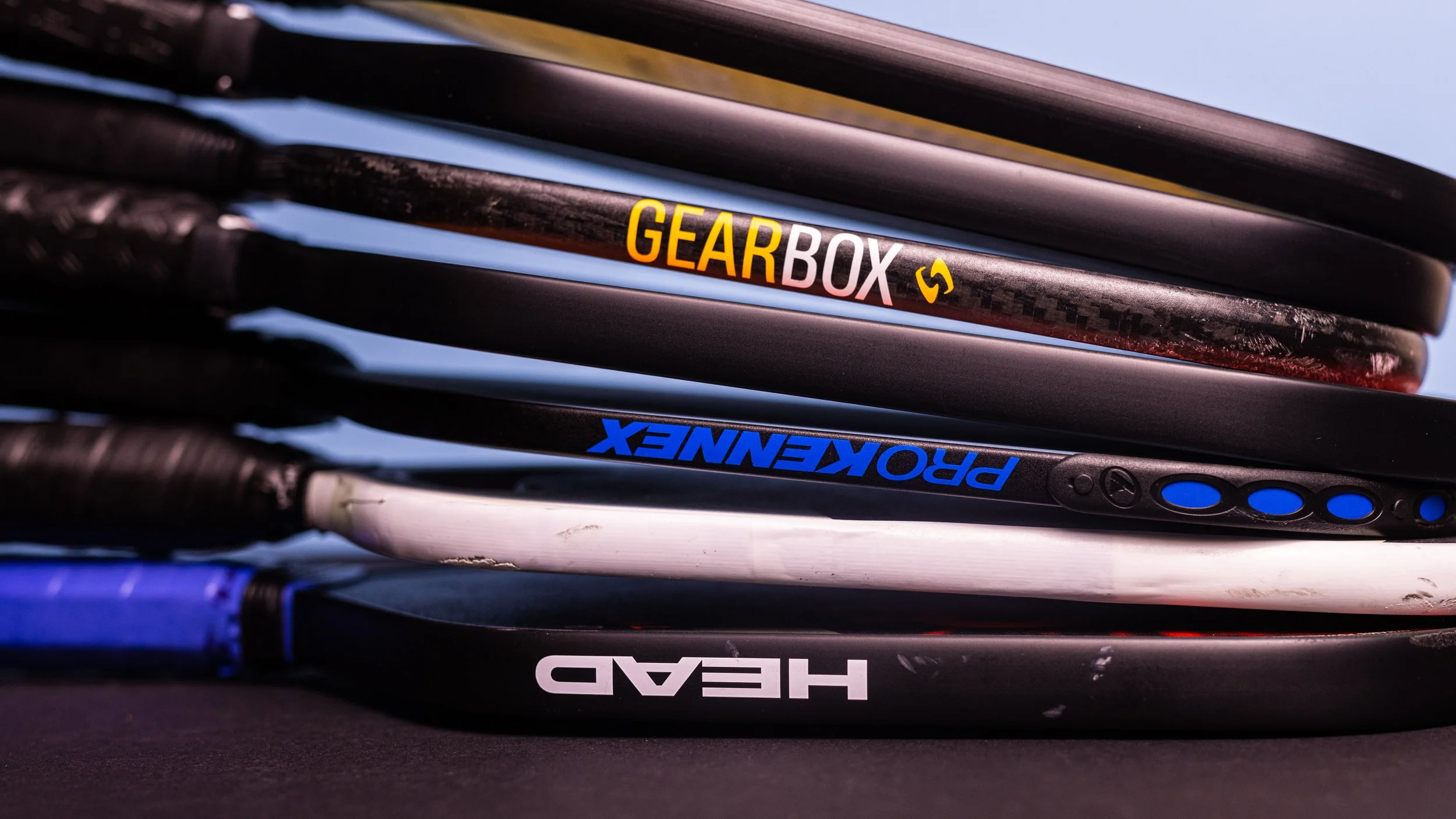 Stack of pickleball paddles from various brands including Gearbox, ProKennex, and Head showing edge profiles