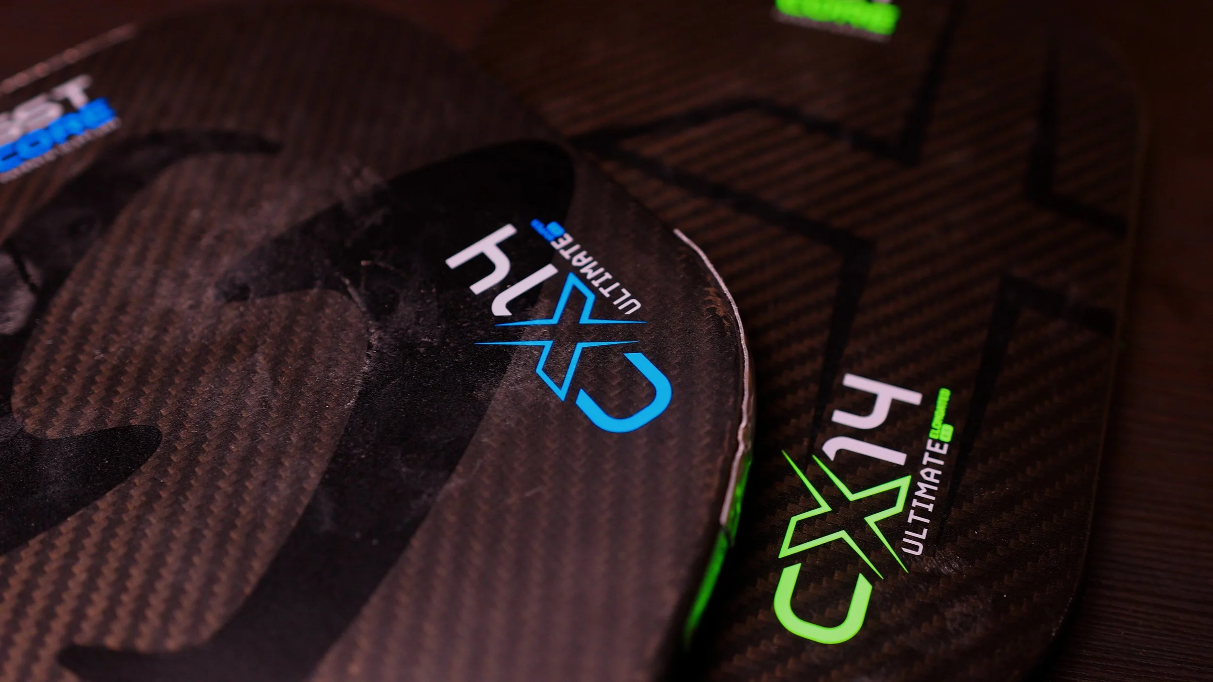 Two Gearbox CX14 Ultimate pickleball paddles in blue and green overlapping on a dark surface