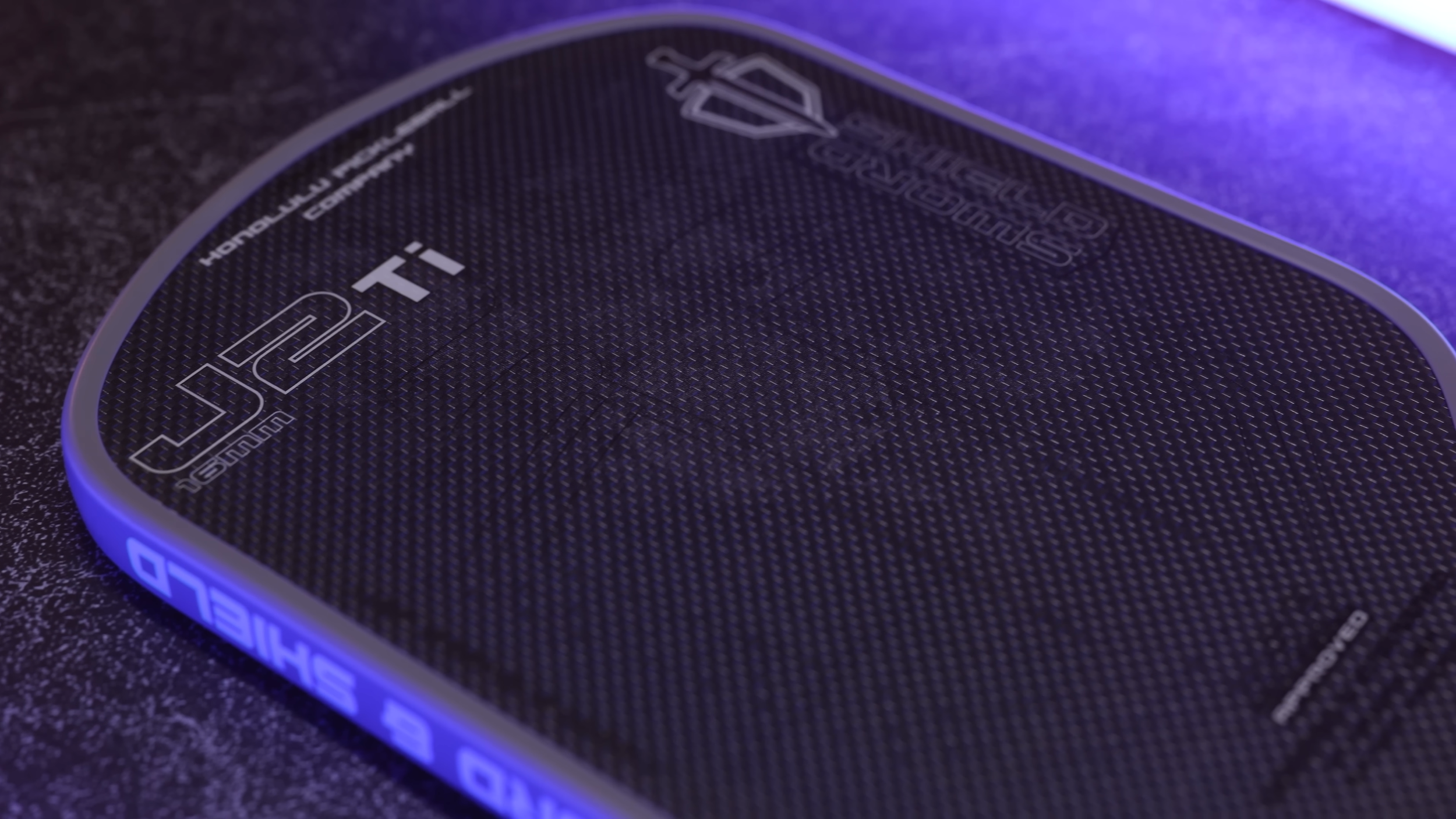 Honolulu J2Ti pickleball paddle close-up showing carbon fiber face texture and Sword & Shield branding