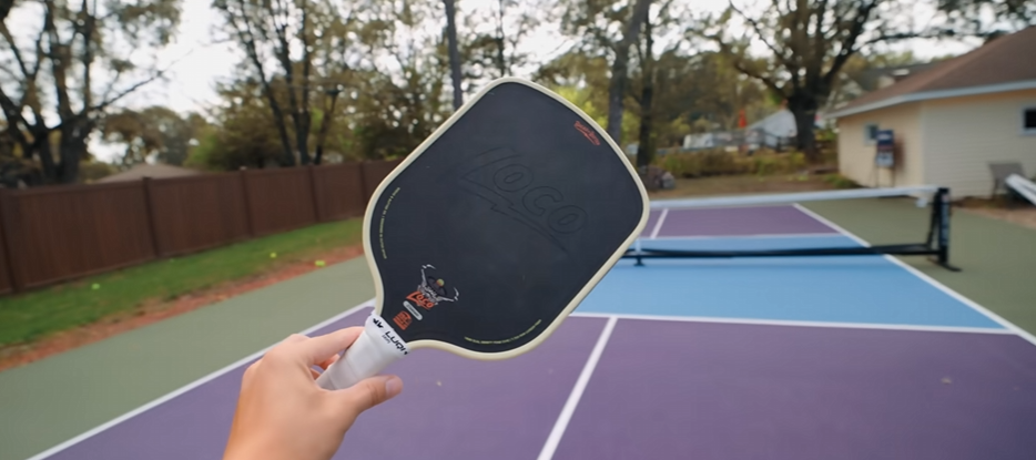 Hand holding the Bread & Butter Loco pickleball paddle face-forward on an outdoor court