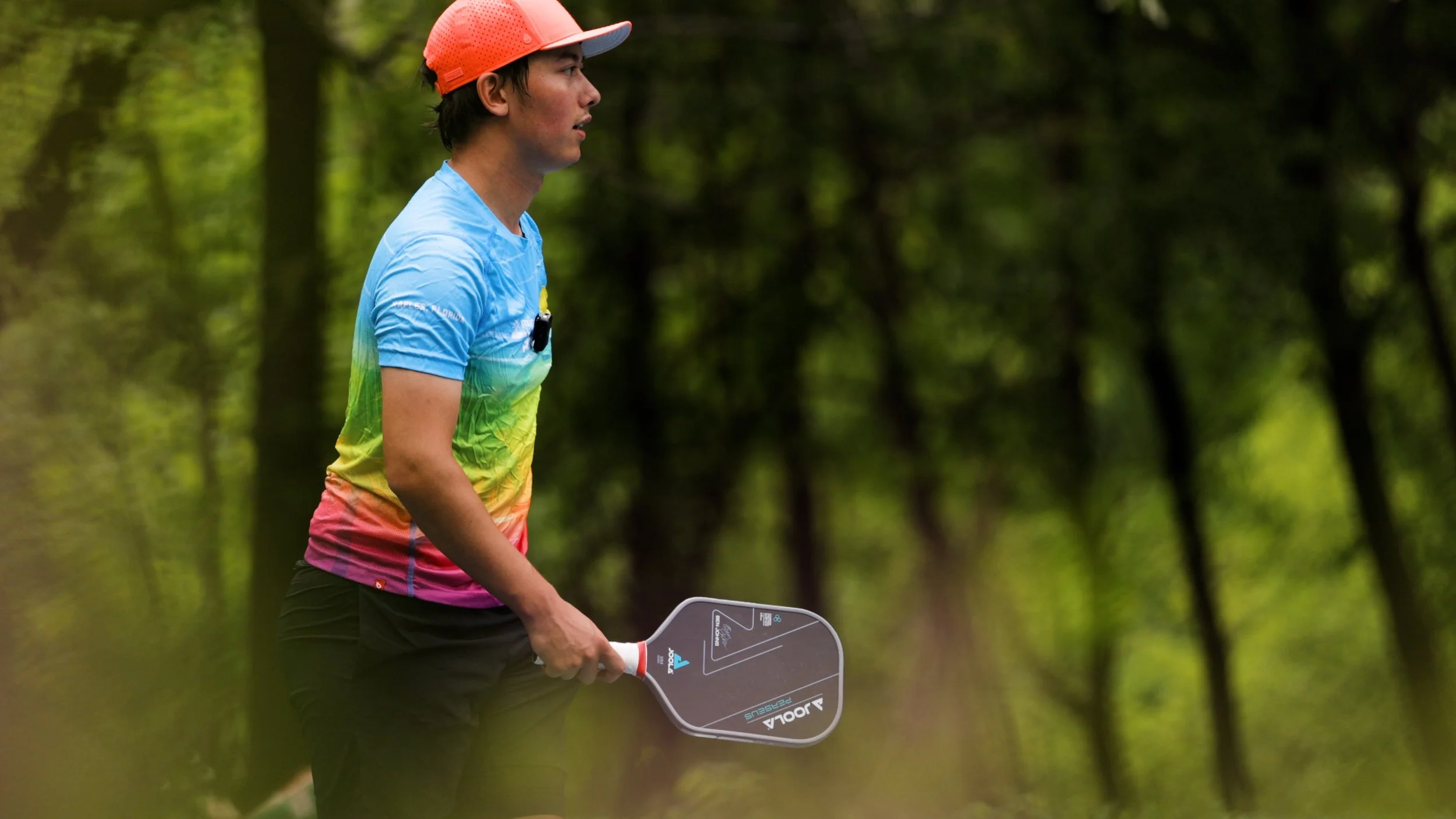Player holding a JOOLA Ben Johns Perseus pickleball paddle outdoors among trees