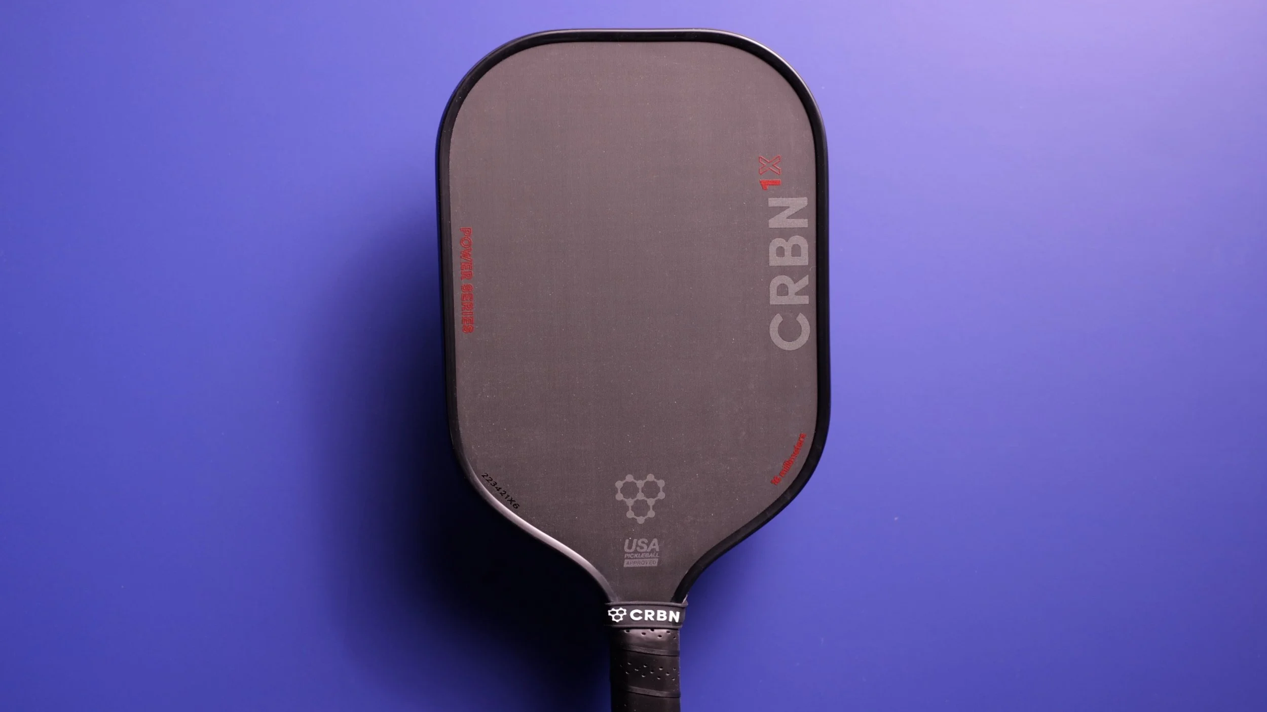 CRBN 1X 16mm pickleball paddle front face view on purple background showing dark carbon fiber surface