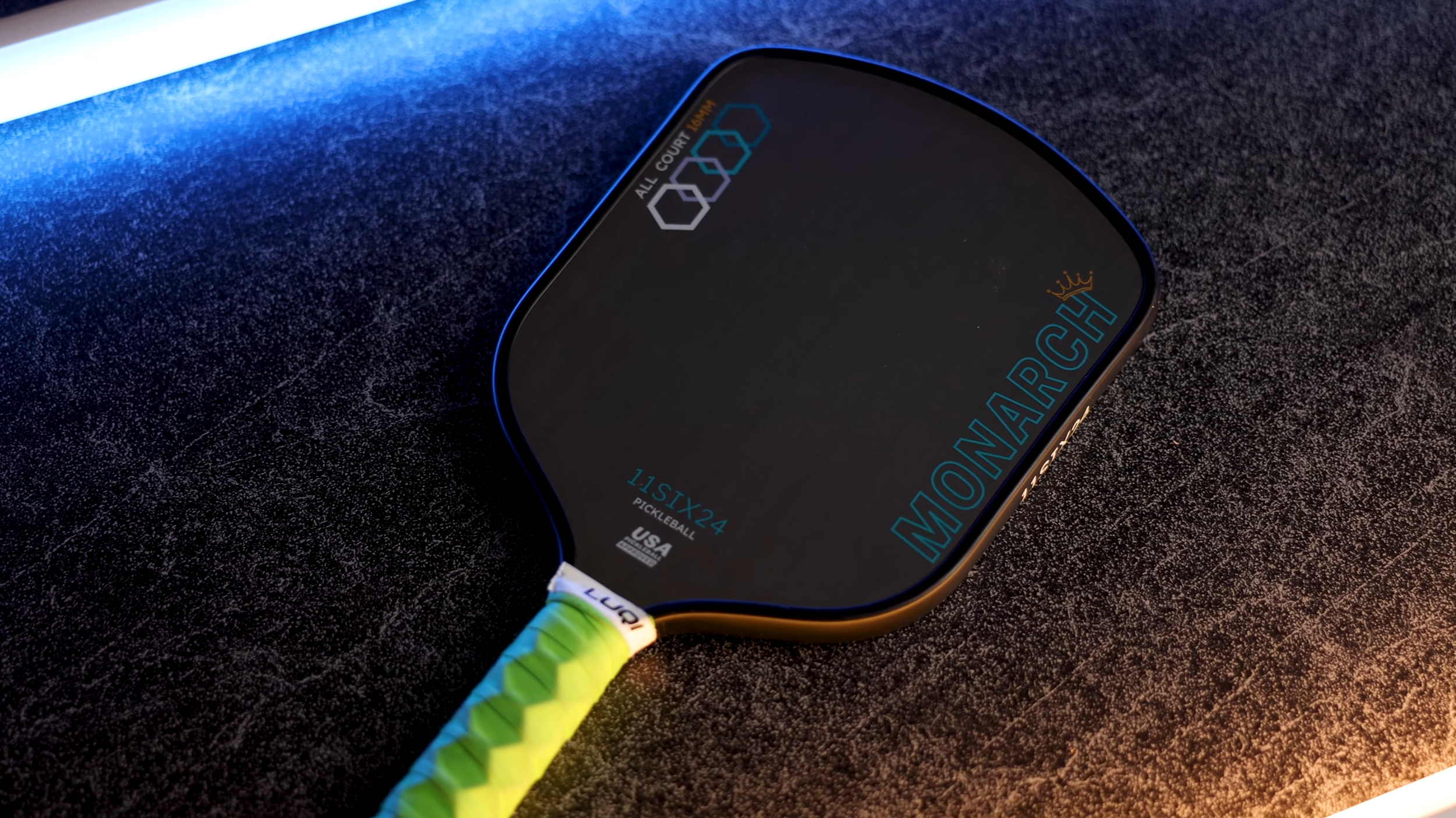 11SIX24 Monarch All Court pickleball paddle close-up showing black face with blue accents and neon green grip