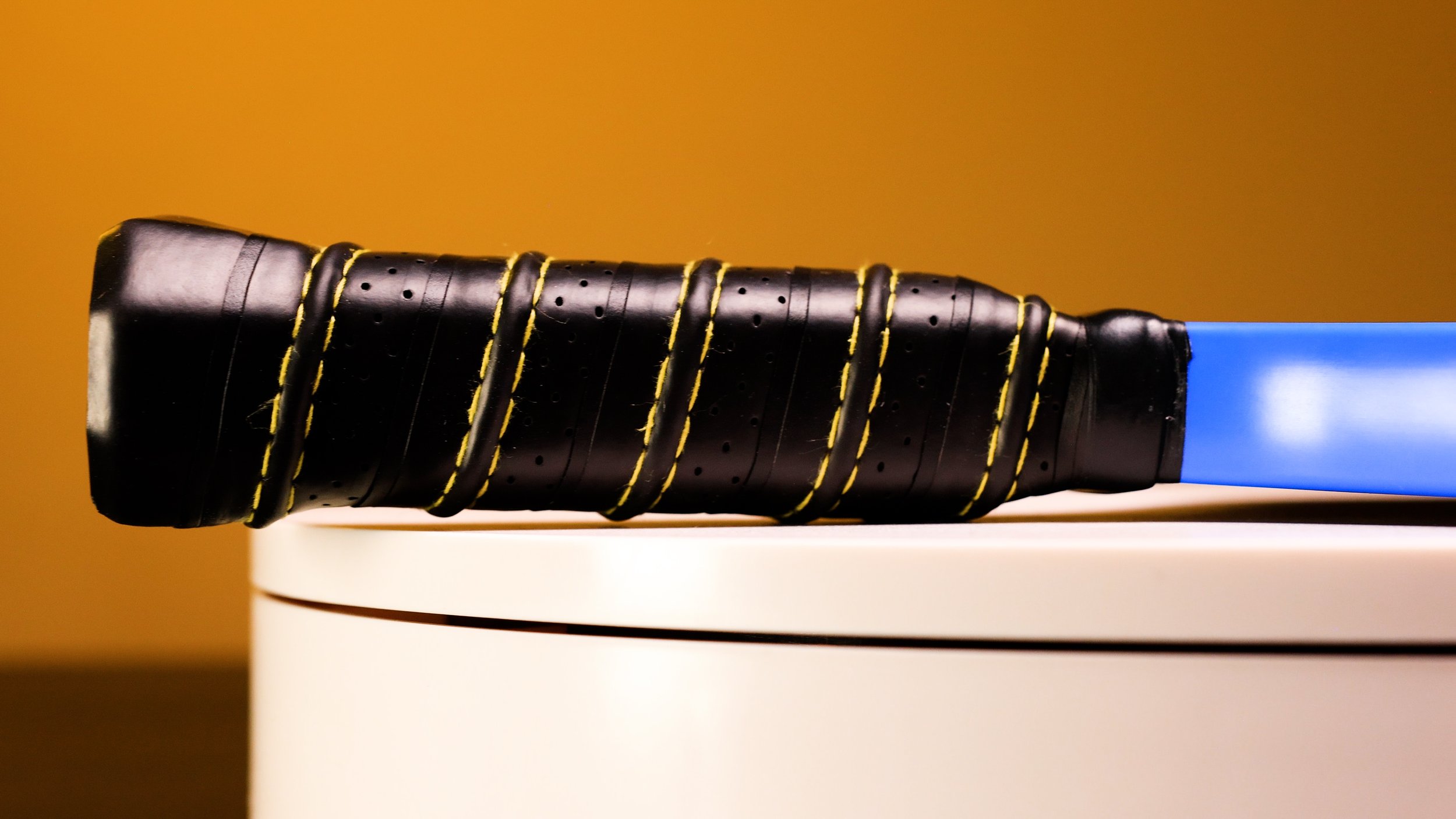Electrum Model E Elite pickleball paddle grip close-up showing perforated black grip with yellow stitching