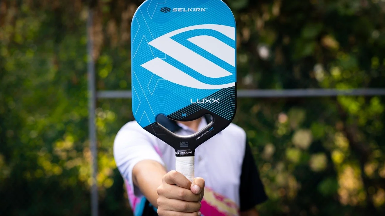 Player holding Selkirk Luxx Control Air pickleball paddle face-forward showing blue design and Selkirk logo