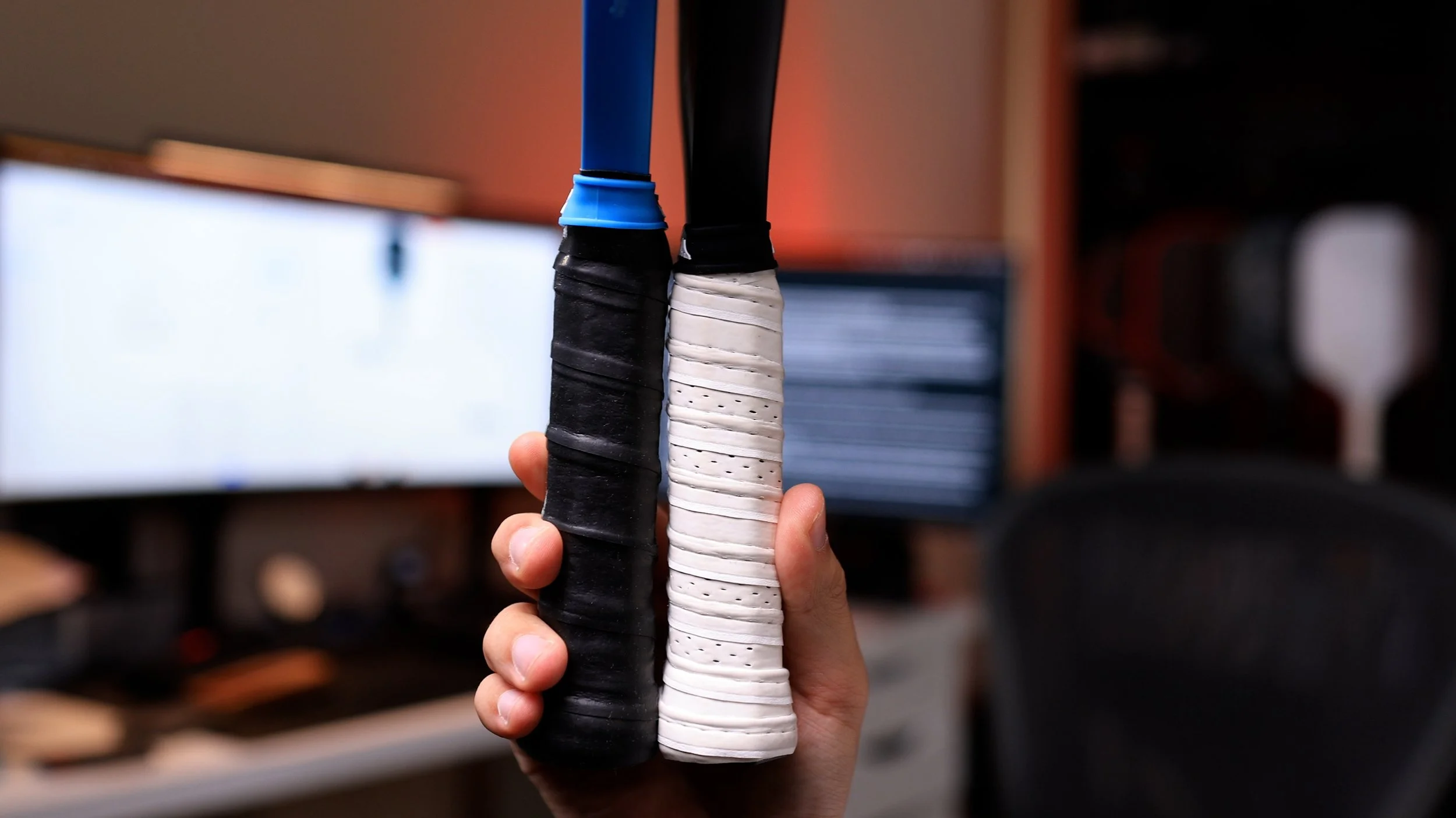 Hand holding two pickleball paddle handles comparing grip sizes with black and white overgrips