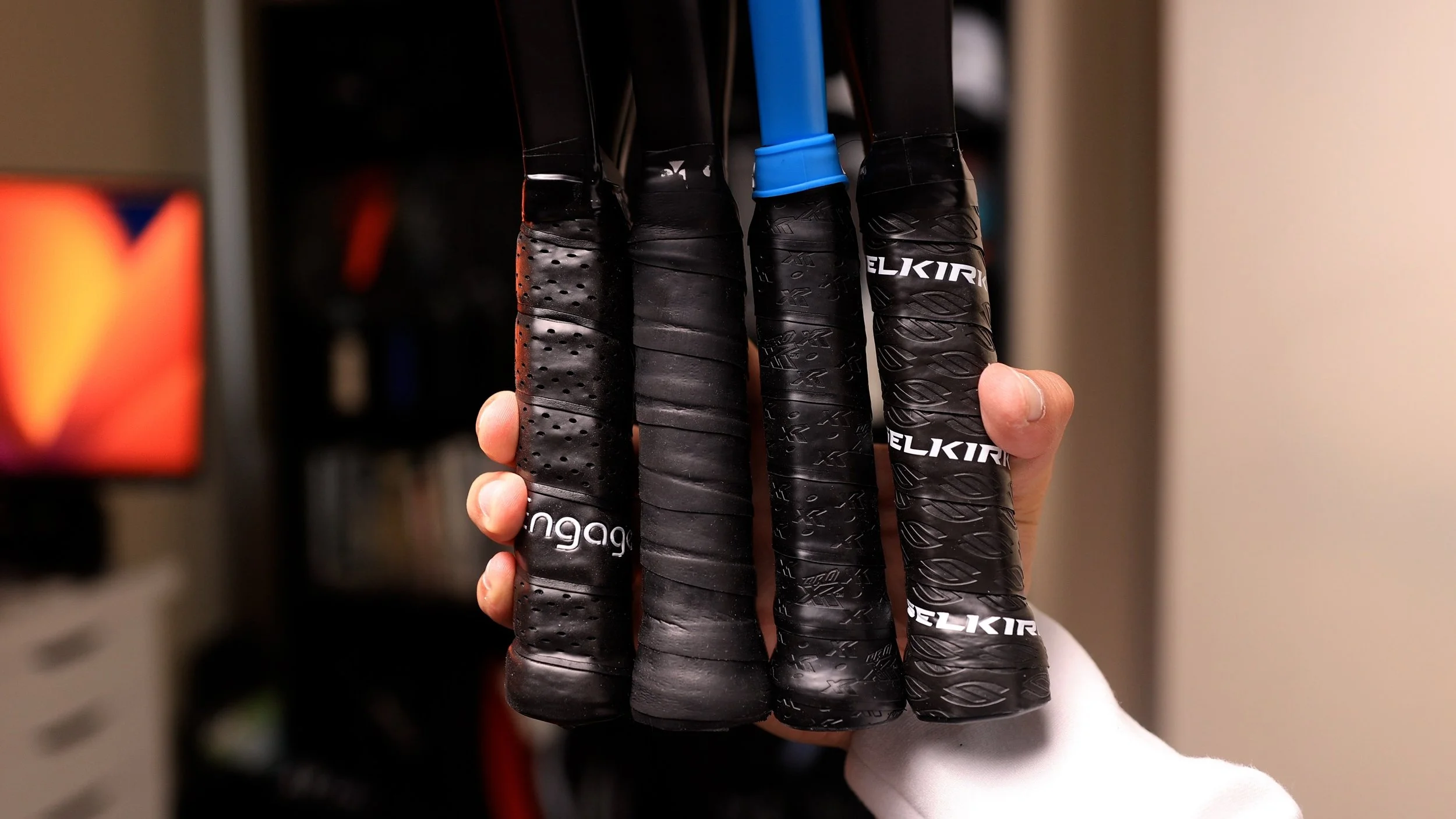 Hand holding four pickleball paddle grips including Engage, Selkirk, and Zane Navratil Signature comparing sizes