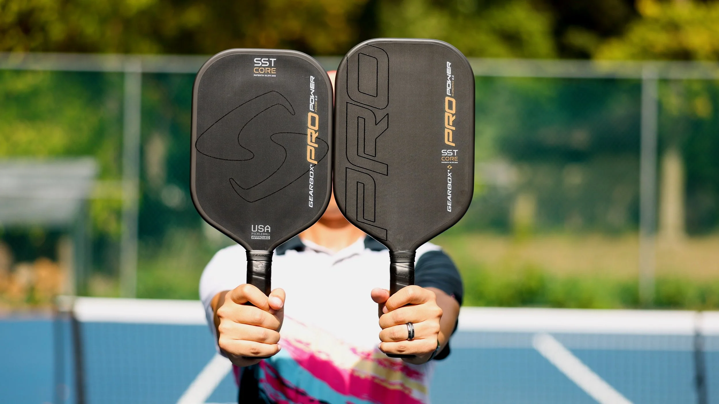 Player holding up two Gearbox Pro Power pickleball paddles in Elongated and Fusion shapes on an outdoor court