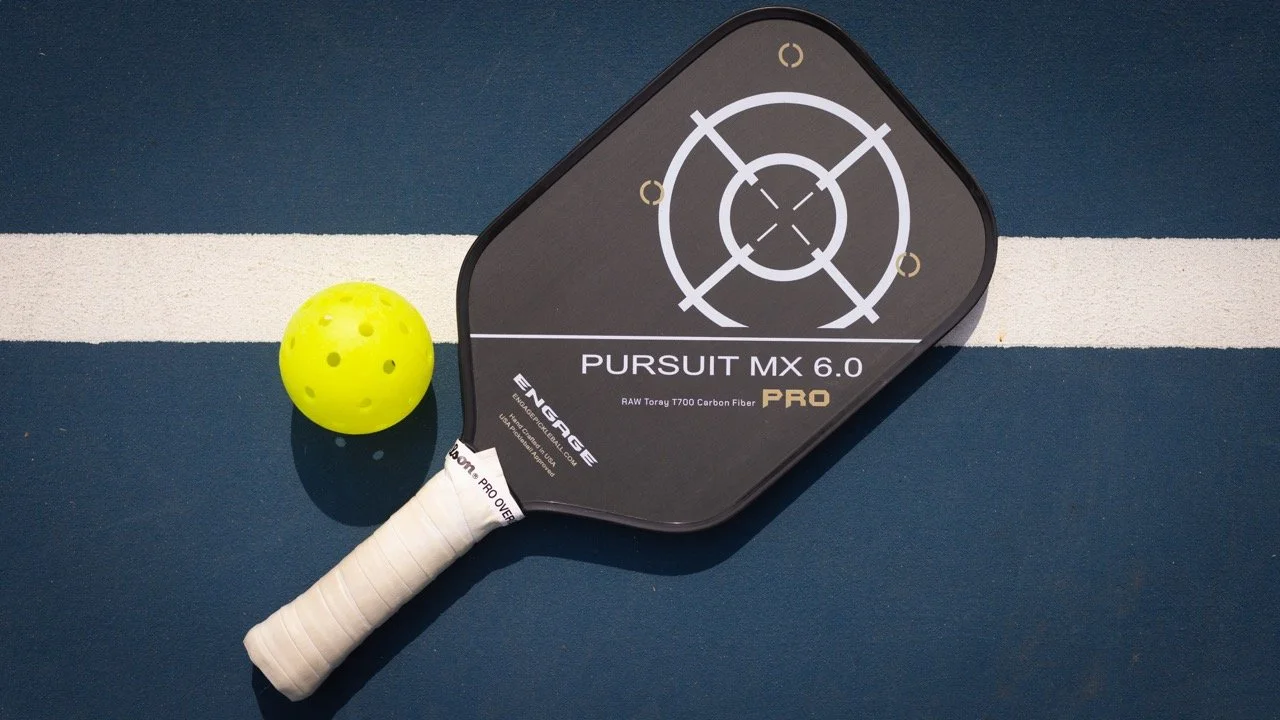 Engage Pursuit MX 6.0 Pro pickleball paddle on a blue court next to a pickleball