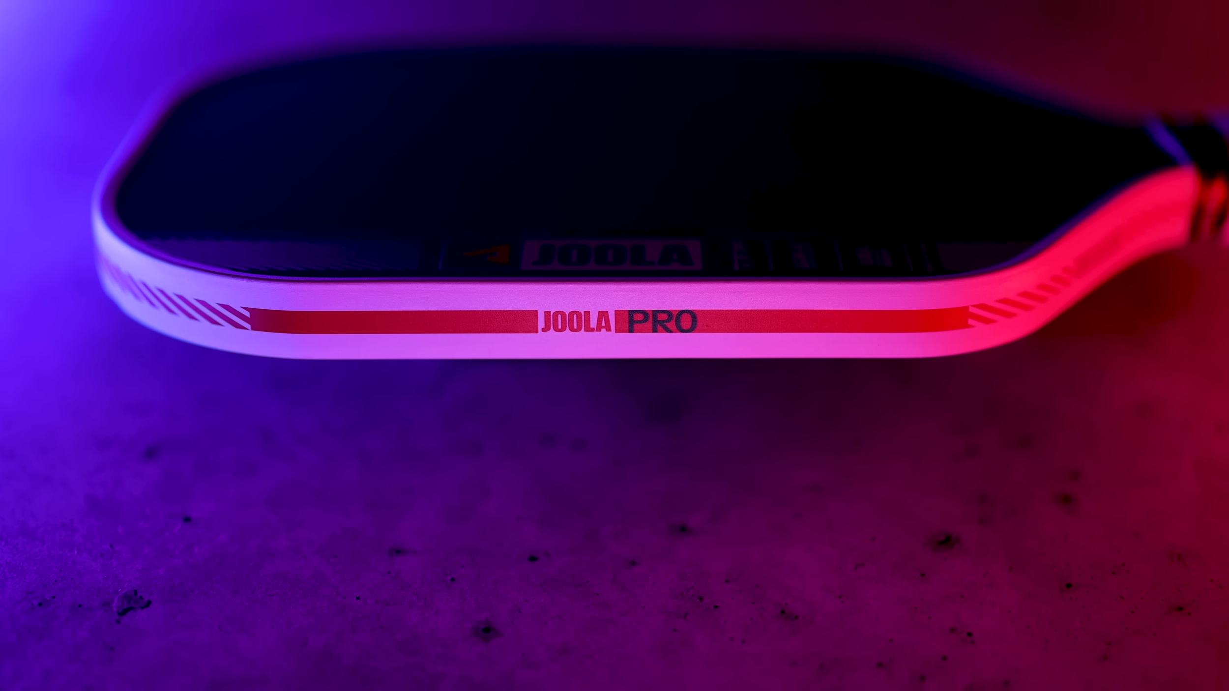 Side view of JOOLA Pro pickleball paddle edge showing the red accent stripe and profile thickness