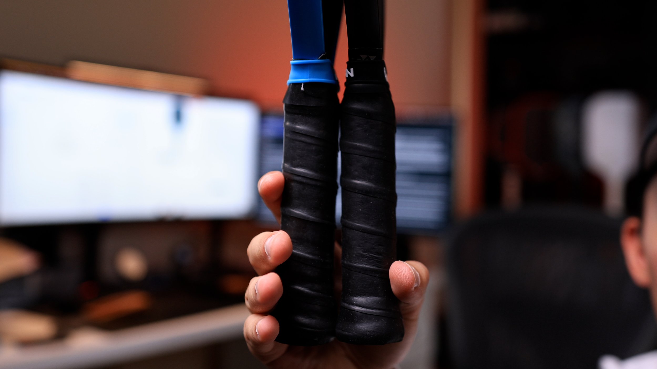 Hand holding two pickleball paddle handles showing bottom view grip comparison