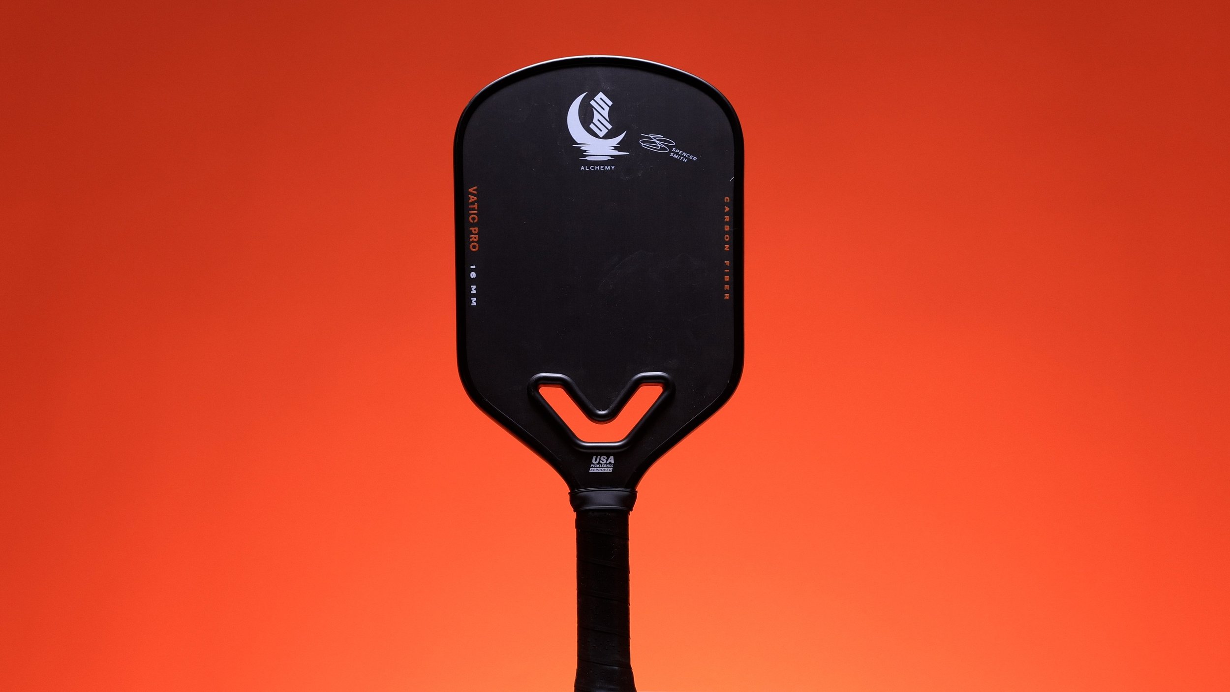 Vatic Pro Alchemy pickleball paddle front view showing V-shaped throat hole on orange background Vatic Pro Alchemy pickleball paddle front view showing V-shaped throat hole on orange background