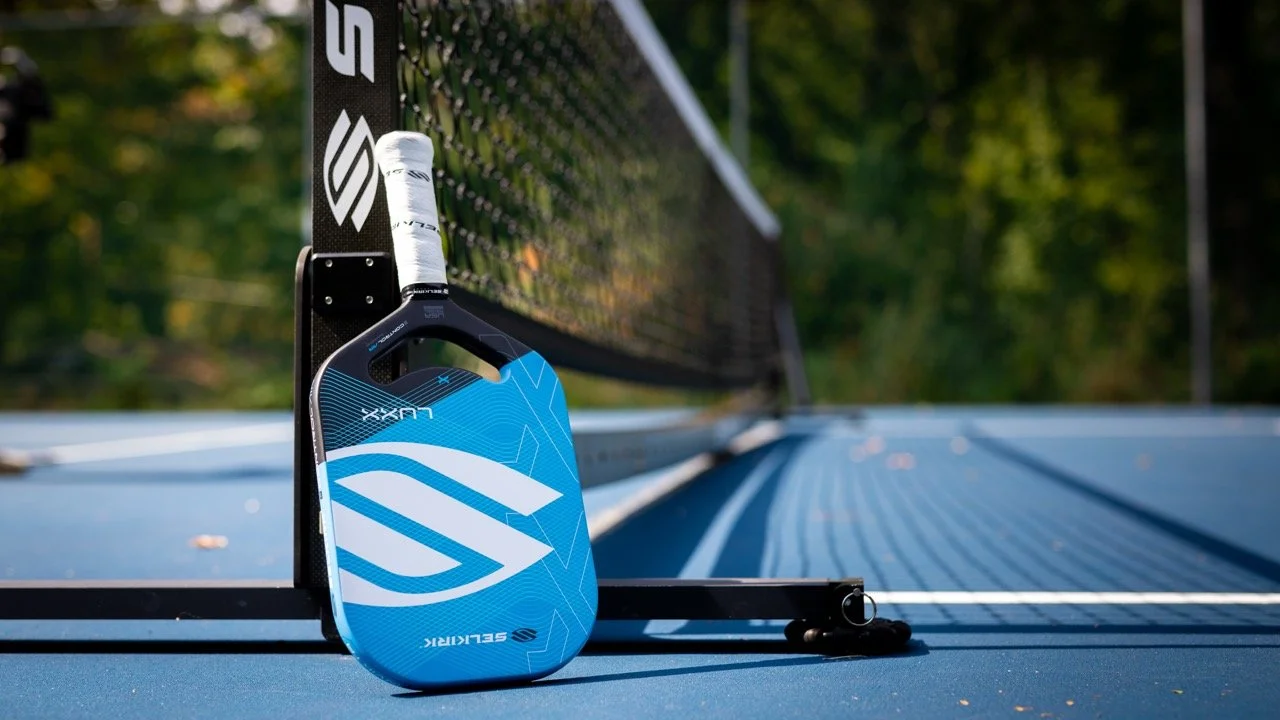 Selkirk Luxx Control Air pickleball paddle in blue leaning against net on outdoor court
