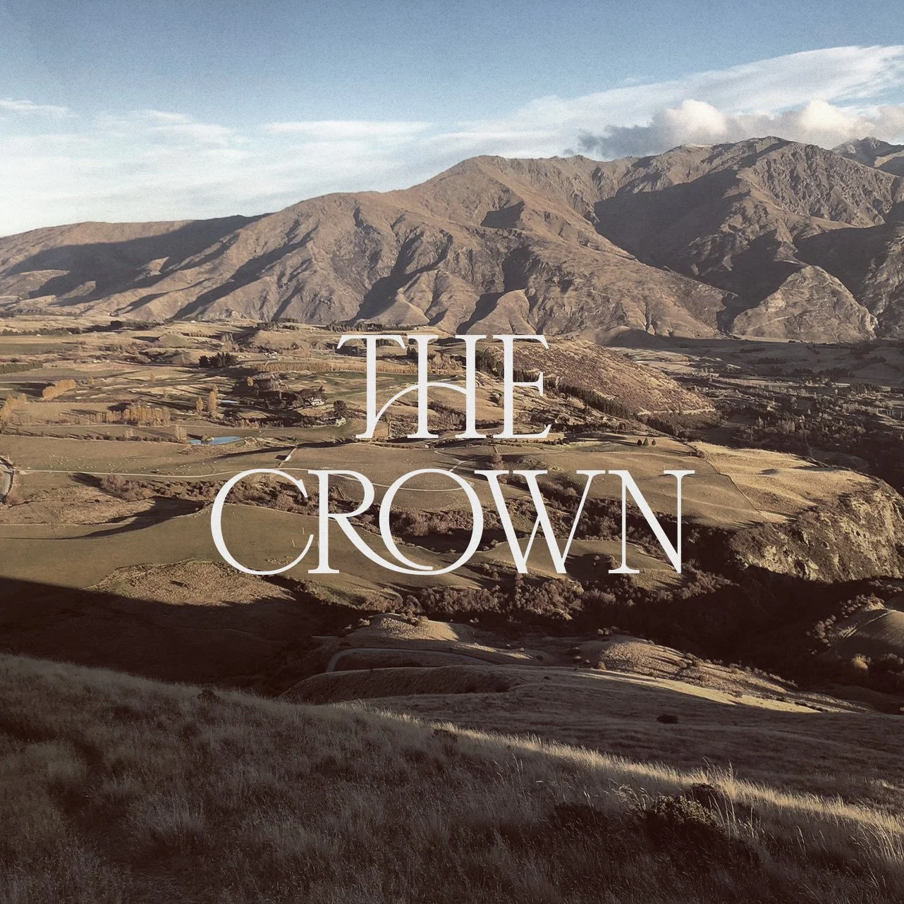 Scenic landscape with rolling hills and mountains in the background, featuring the text 'The Crown' in large letters across the image.