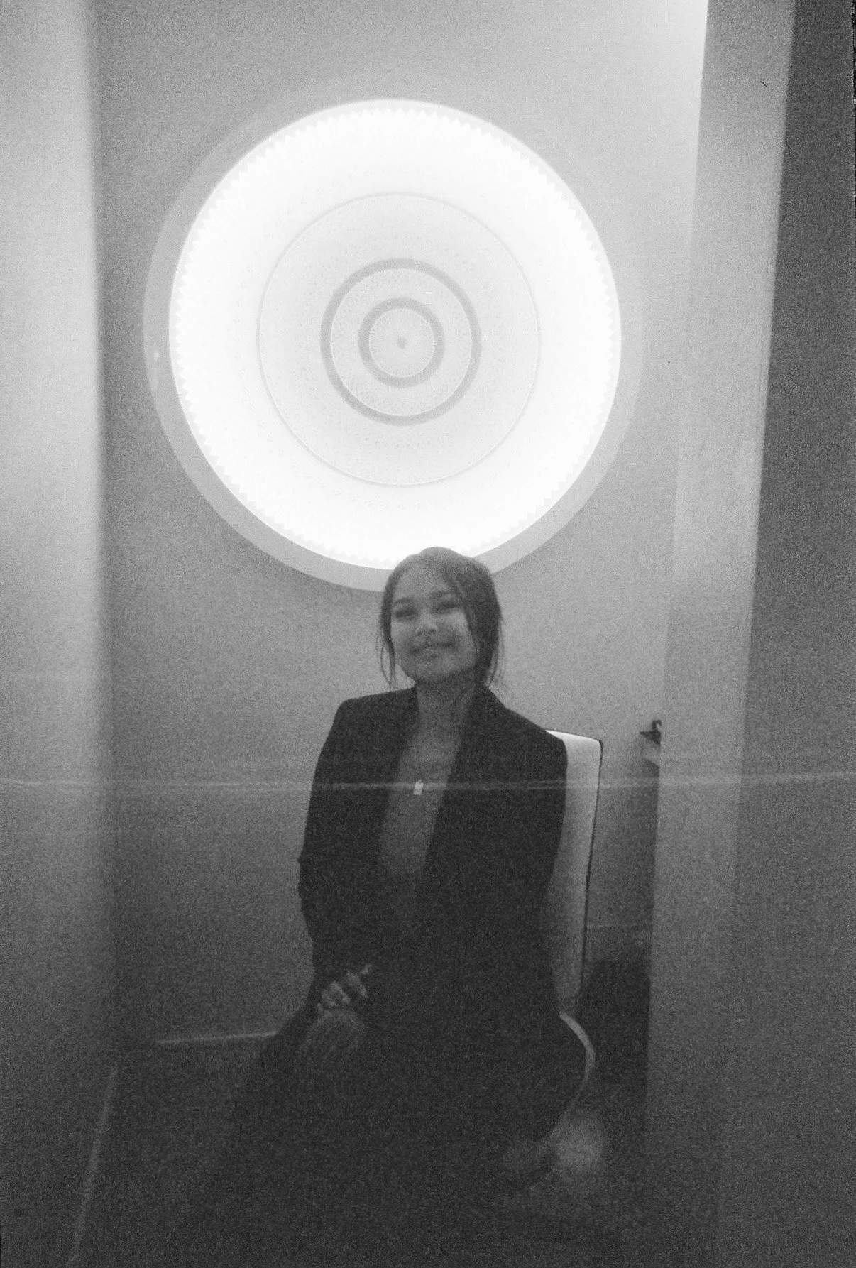 Woman sitting in a chair under a circular light fixture, black and white photo.