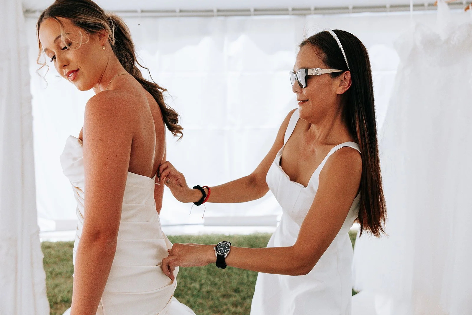 A bride getting help with her wedding dress, while another person adjusts the back of the gown.