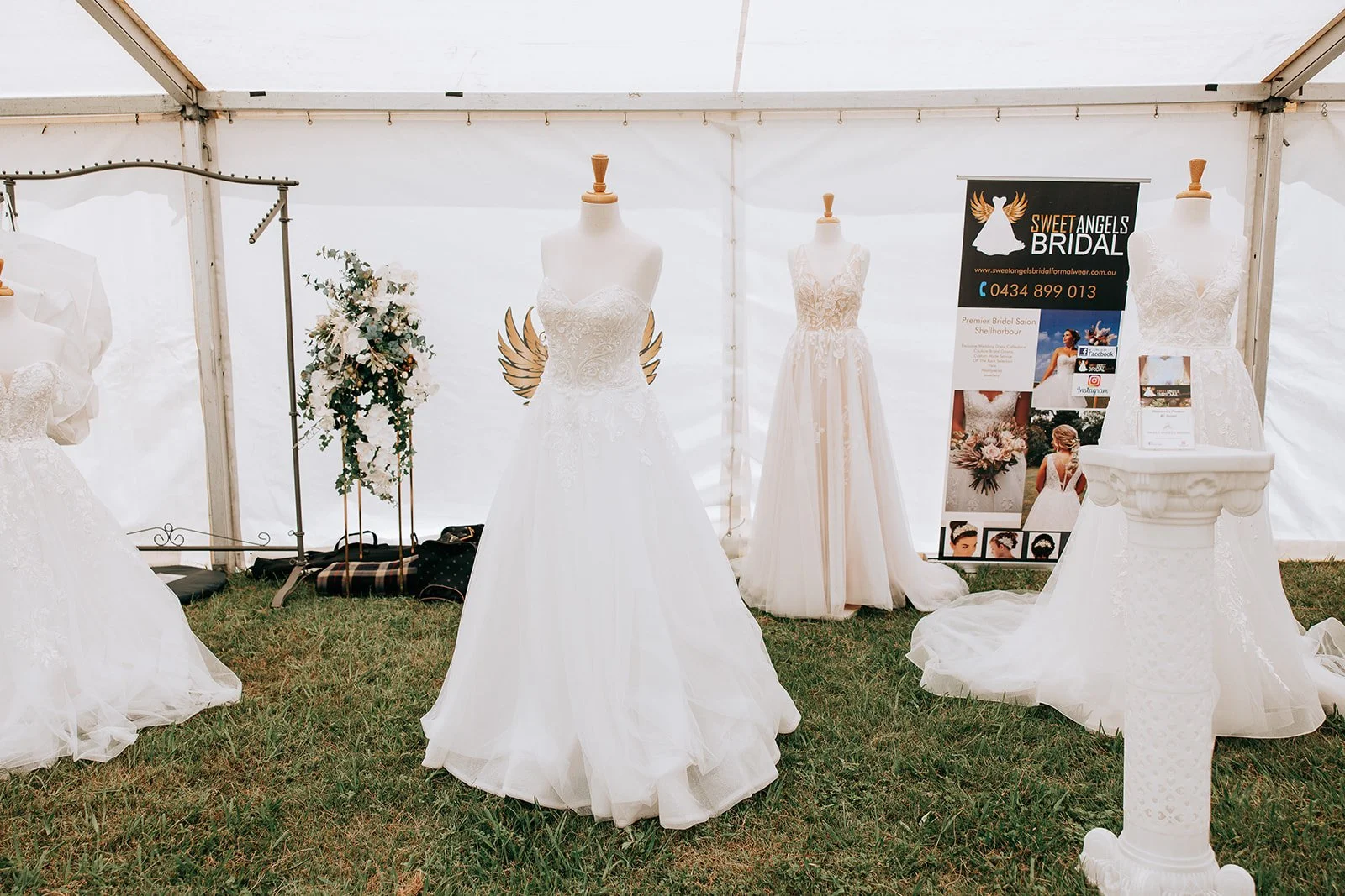 Various bridal gowns displayed on mannequins at a wedding expo, with a Sweet Angels Bridal banner in the background.