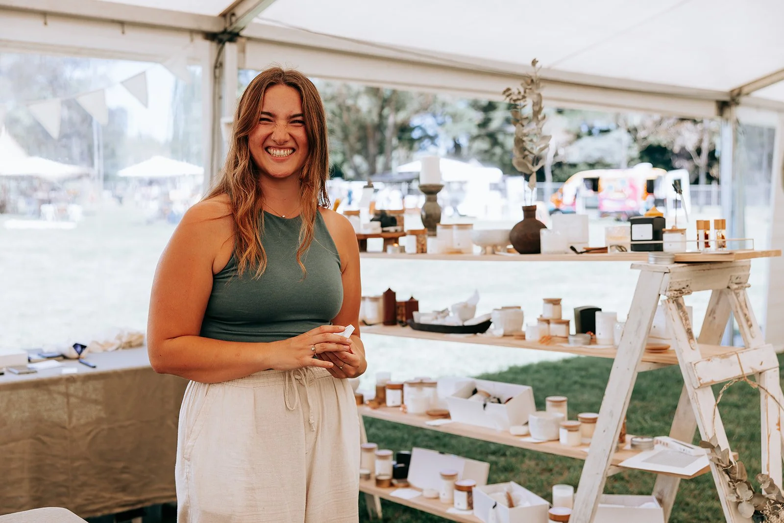 Woman smiling next to a display of handmade candles in a market stall.