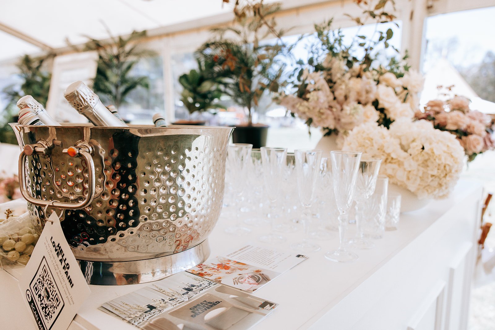 Ice bucket with bottles, champagne flutes, and flowers on a table.