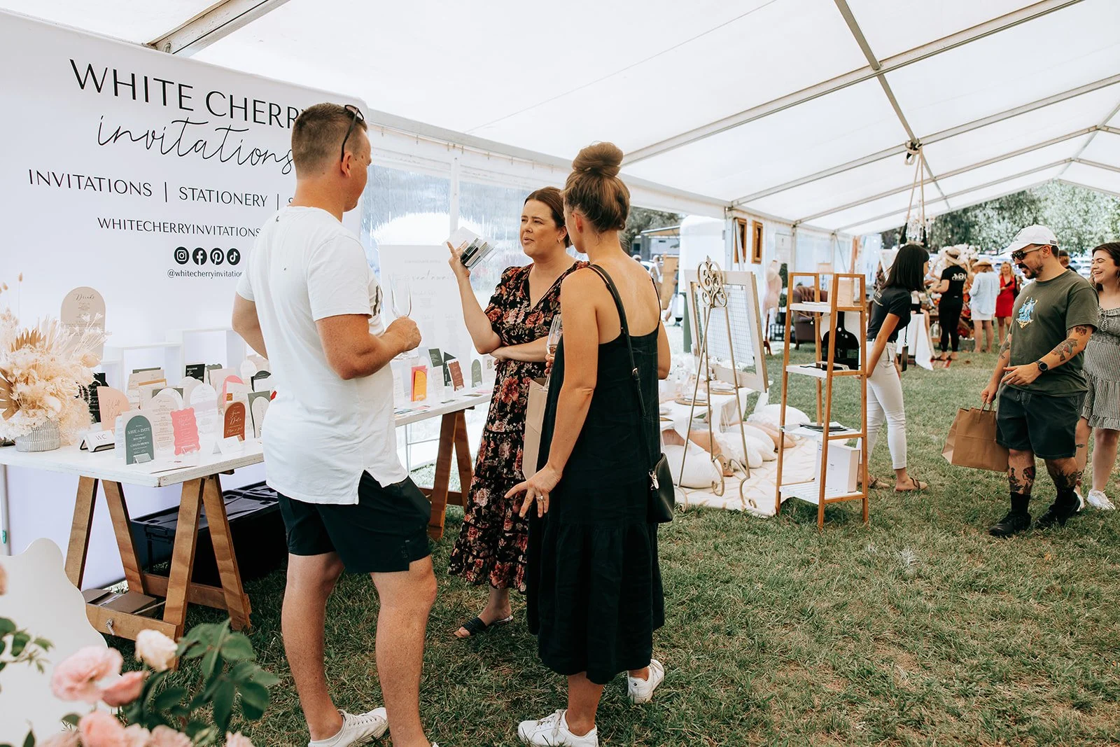 Outdoor event showcasing an invitation and stationery booth with people browsing and interacting.