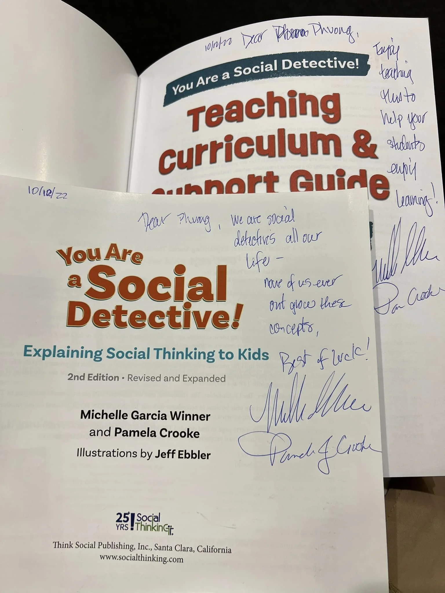 Open book titled "You Are a Social Detective!" and handwritten notes on the pages, including signatures and a date of October 12th, 2022.