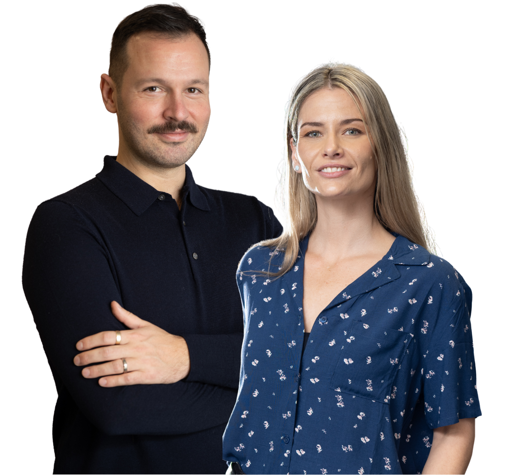 A man with a mustache and a woman with blonde hair standing close, smiling, with a black background.