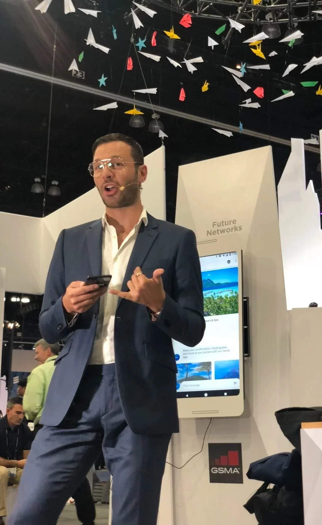 Andrew Charles Edwards, co-founder and CEO of designACE, holding a phone with a lapel microphone, speaking at a conference.
