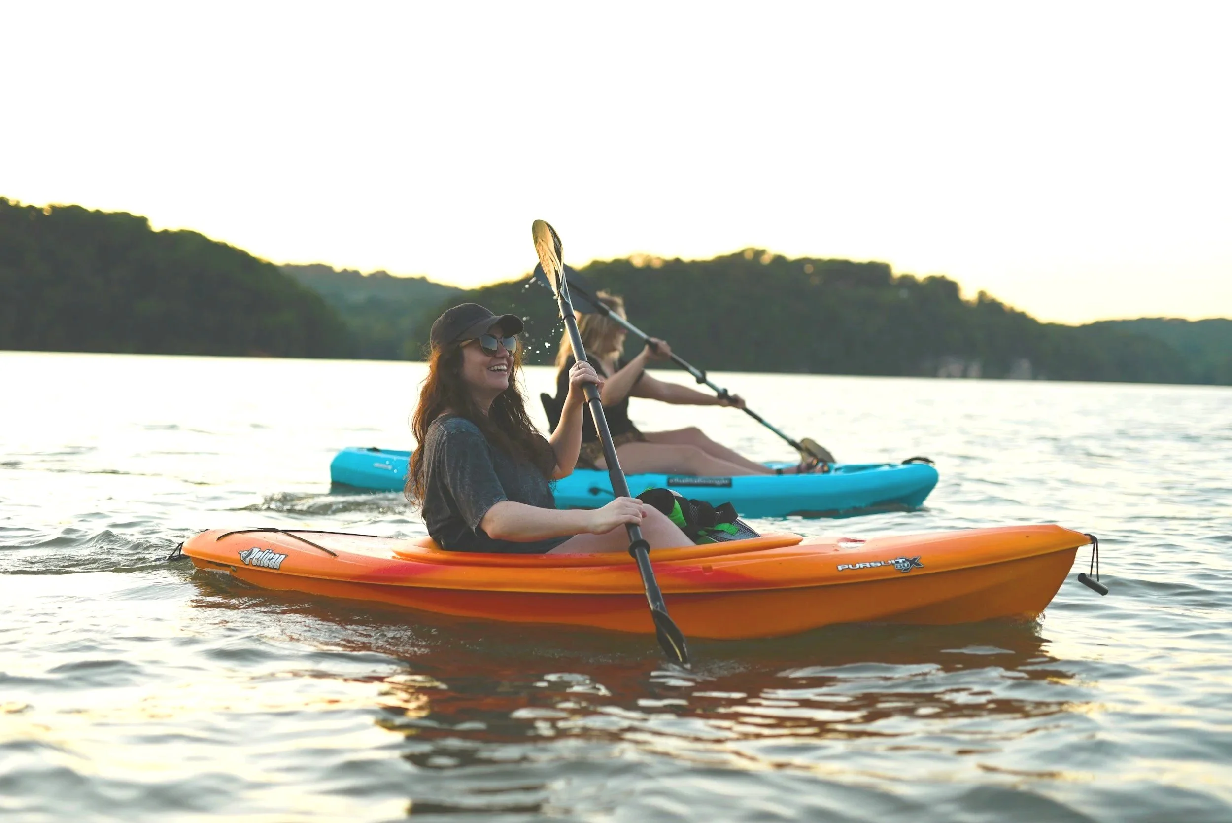 Person kayaking on a lake with fishing rods attached to the kayak, surrounded by greenery.