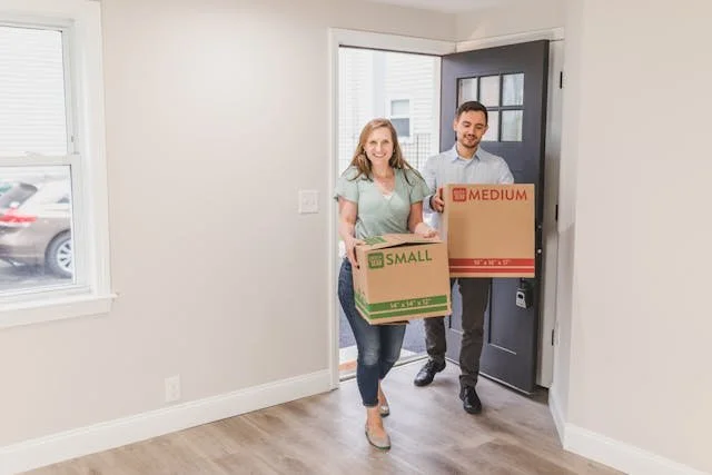 Couple moing into a new home, carrying boxes through the doorway, symbolizing the start of relocating to a new city.