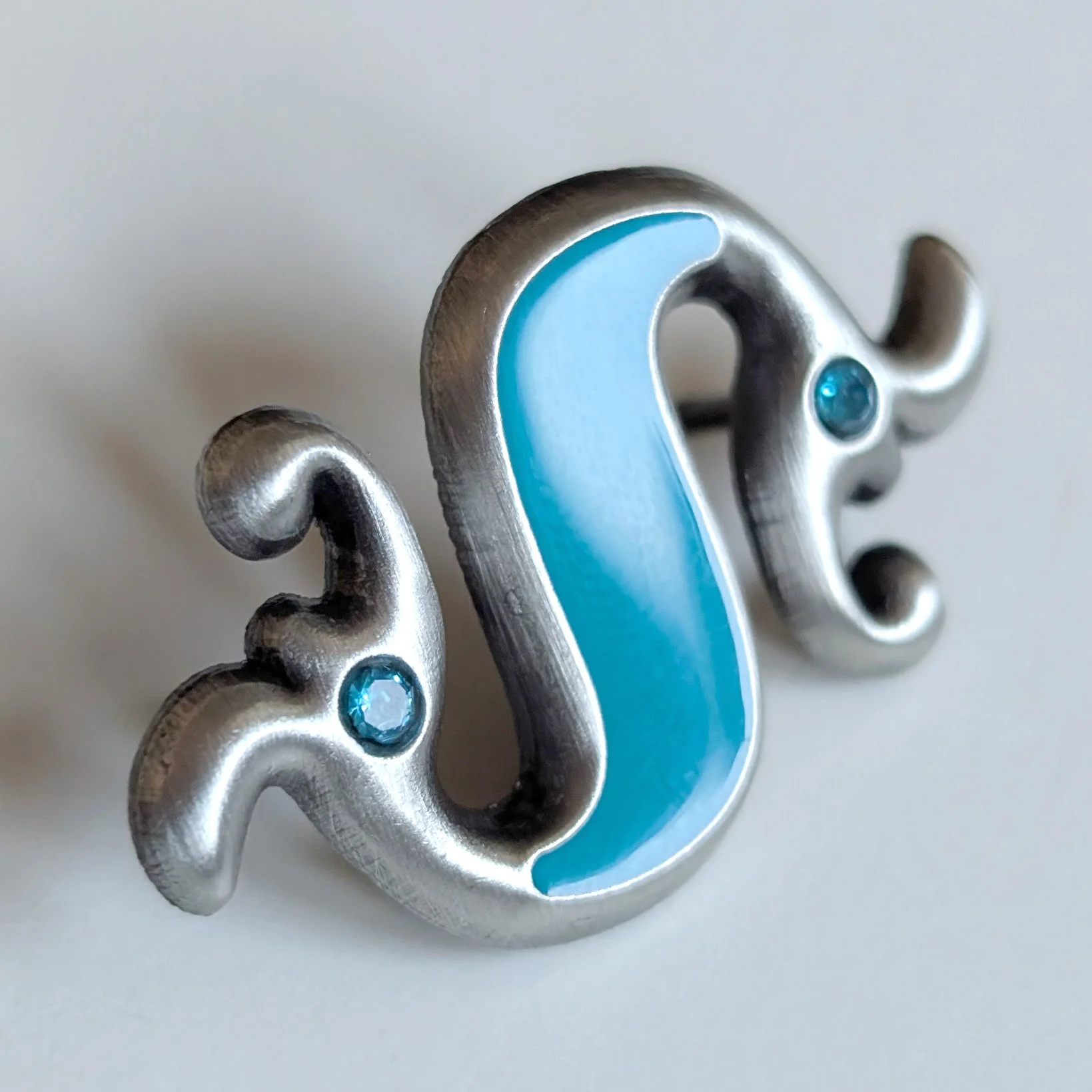 The silver dragonesque brooch at an angle highlighting it's reflections and sparkle