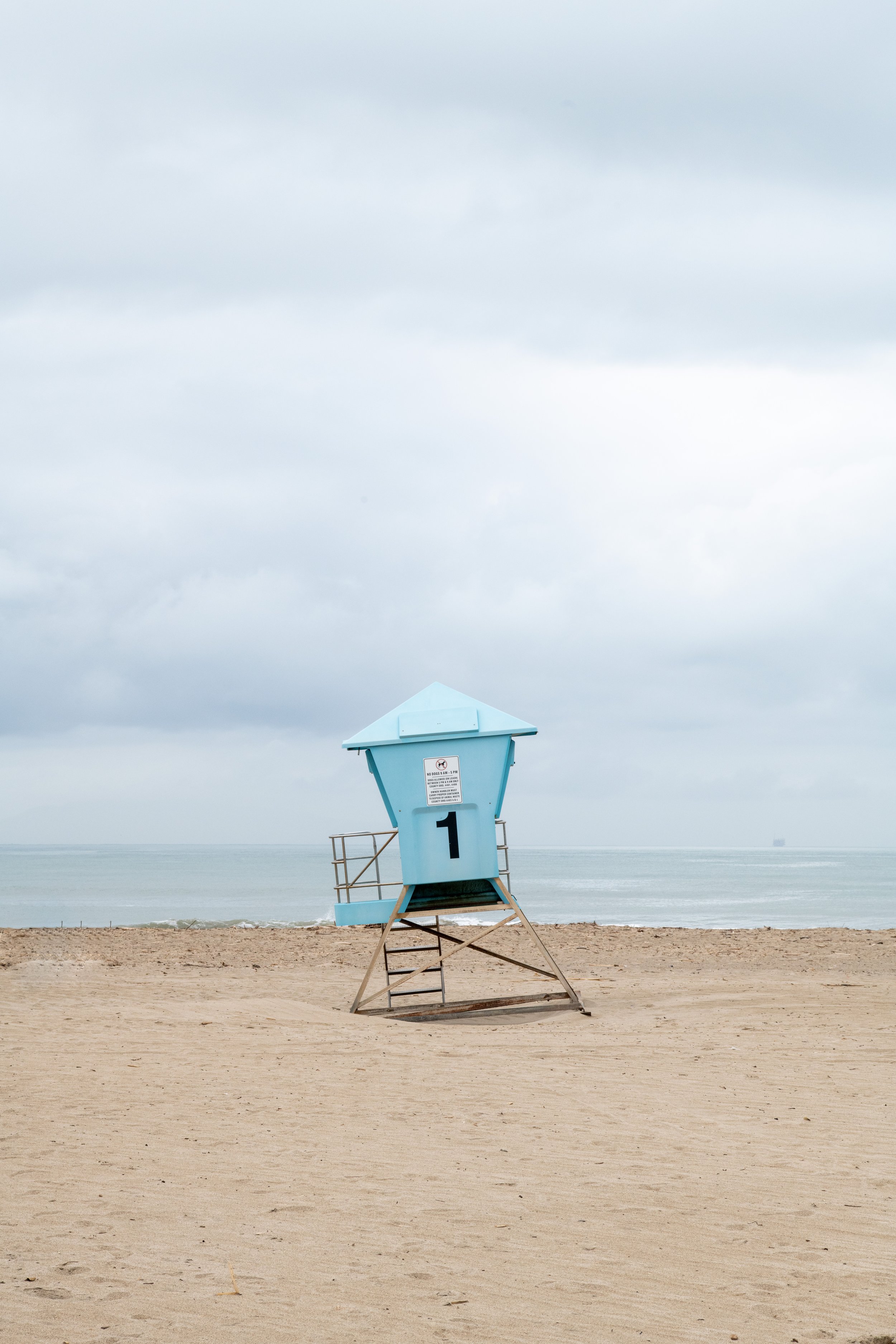 A lifeguard tower on a sandy beach under a cloudy sky, with the ocean in the background.