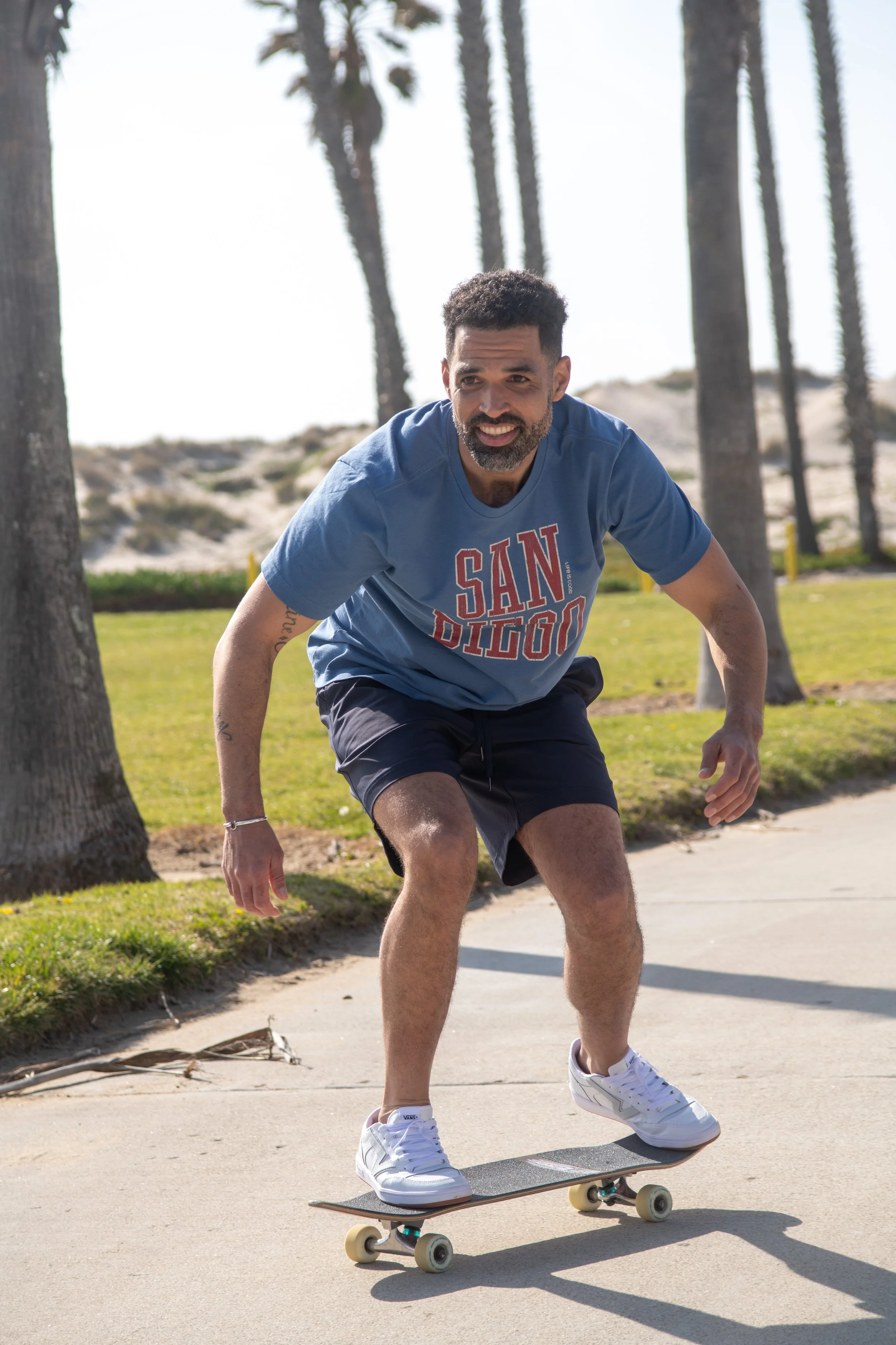 Man skating on a concrete path surrounded by palm trees and grassy areas on a sunny day.