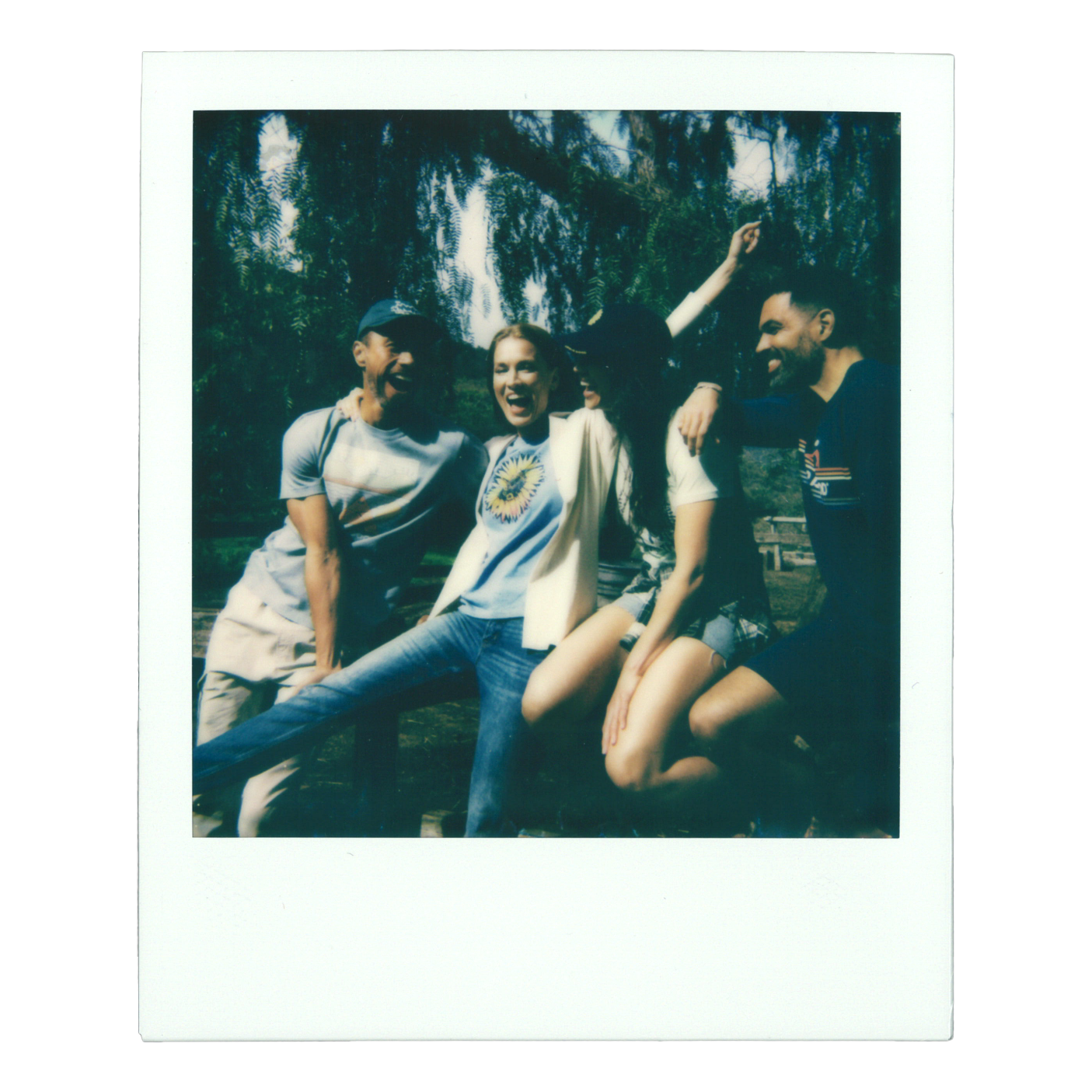 Four young friends laughing and having fun outdoors in a park with trees in the background.