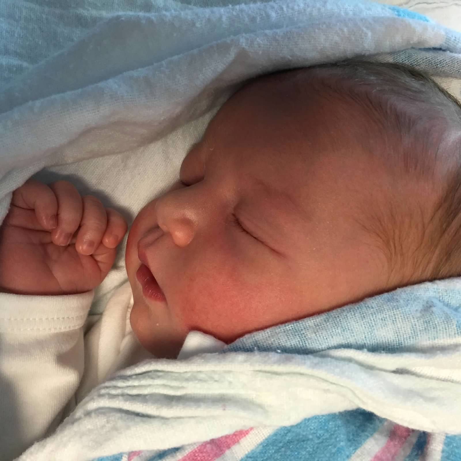 Newborn baby sleeping wrapped in a hospital blanket.