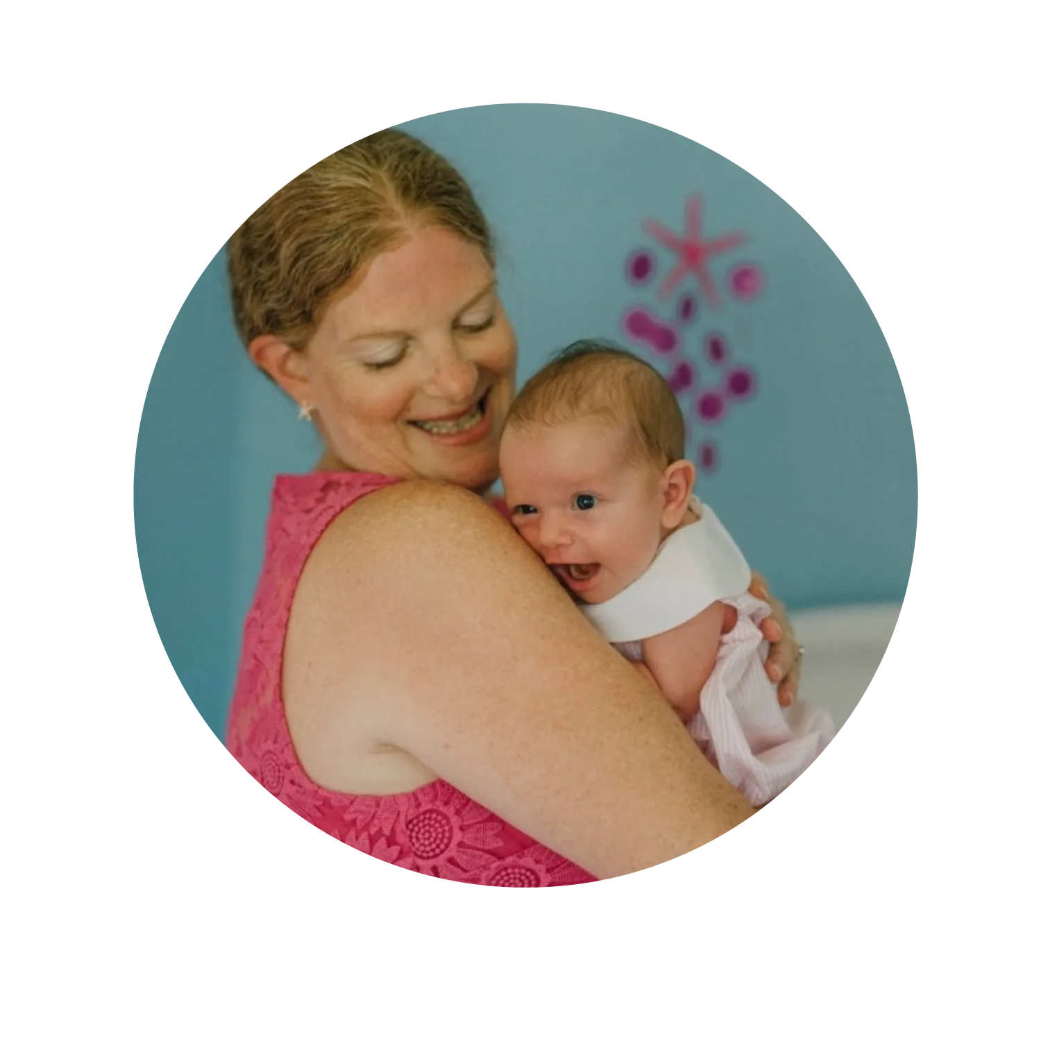 Woman smiling while holding a happy baby in a blue room with pink wall decorations in Alexandria, VA.