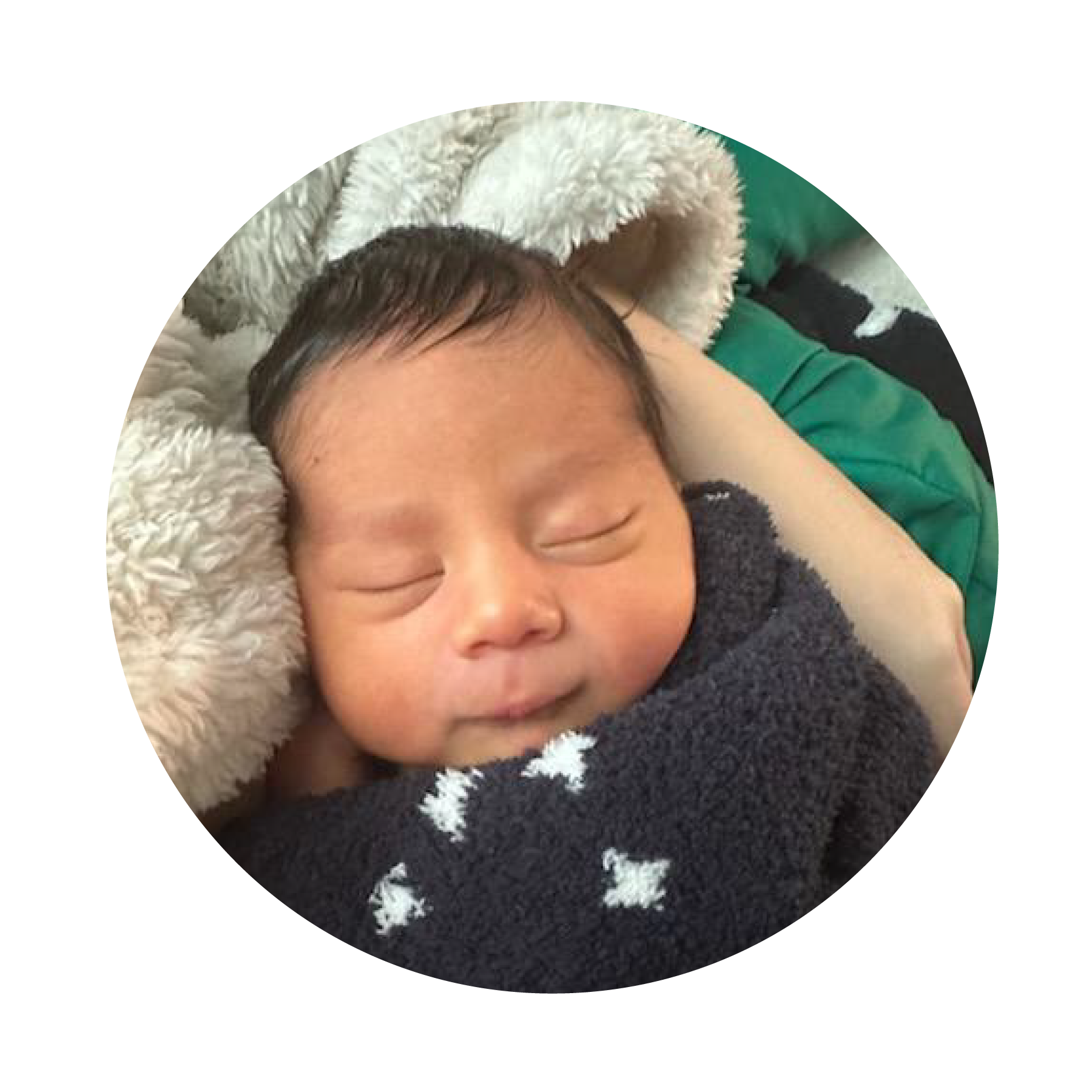 A sleeping newborn baby wrapped in a soft, dark blanket with white stars, resting on a fluffy pillow.
