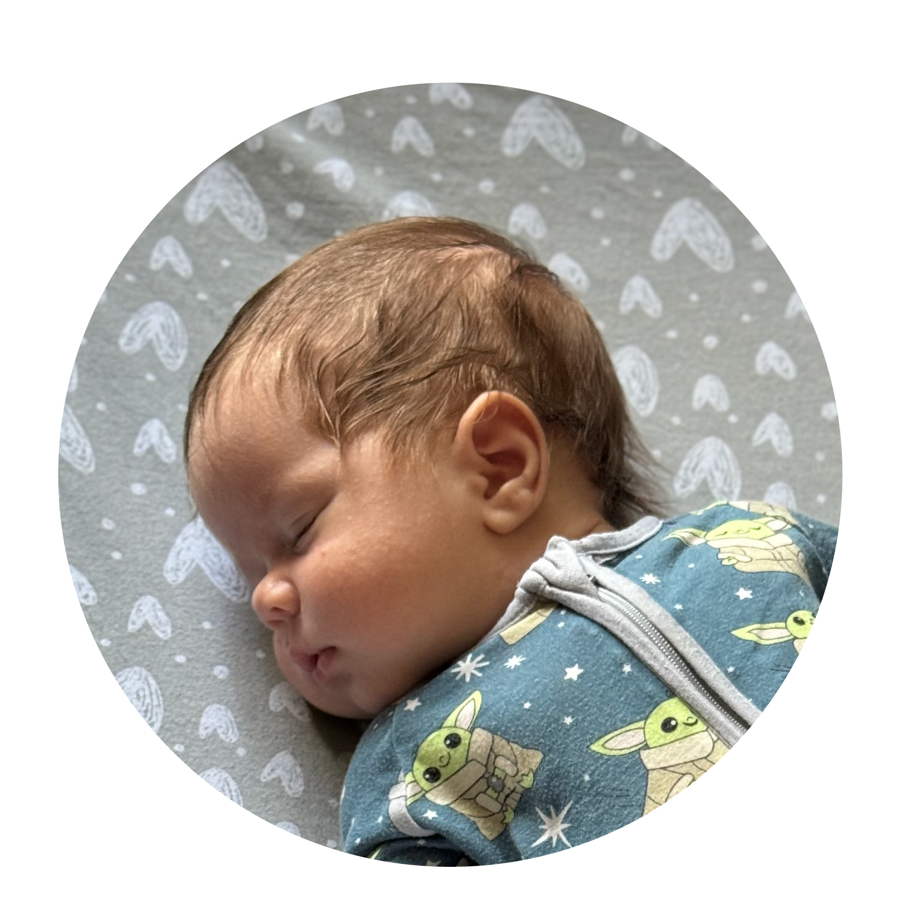 A sleeping baby wearing a blue onesie with a cartoon character pattern, lying on a patterned blanket.