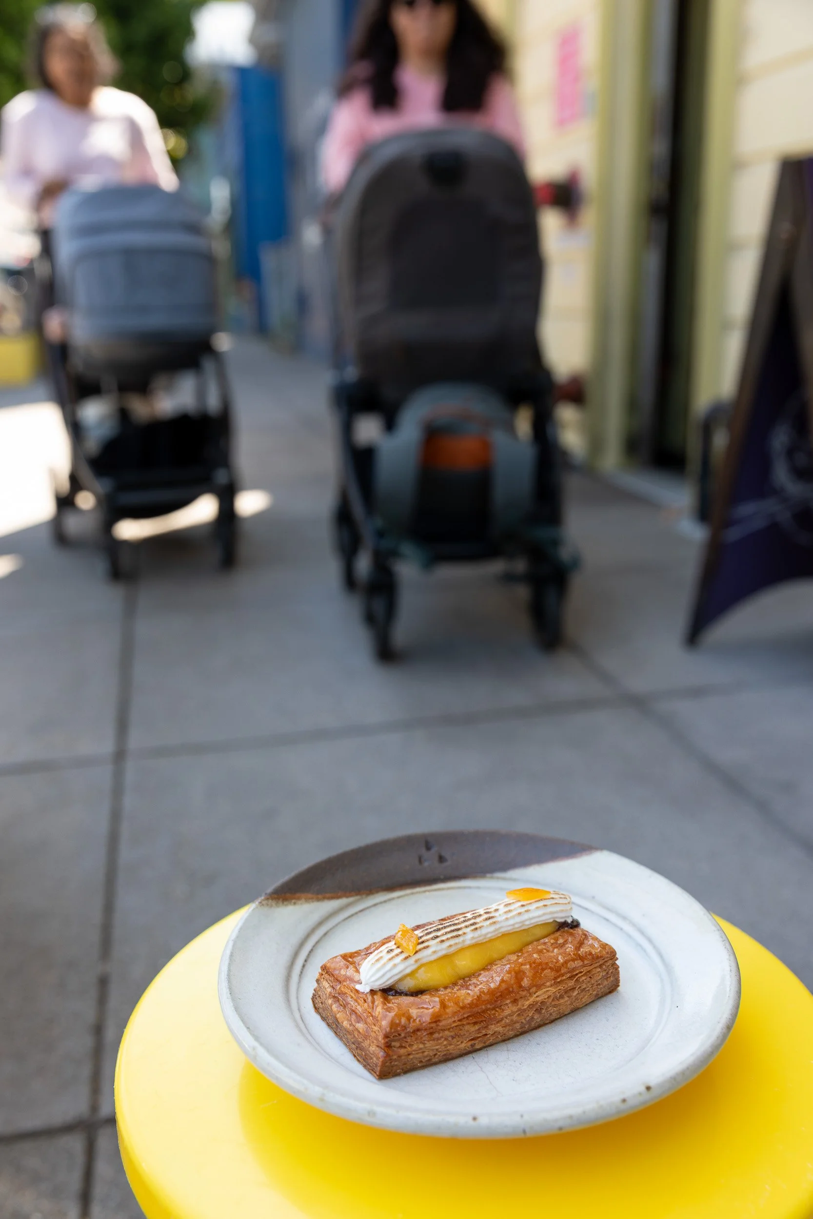 A delicious lemon pastry in the foreground, with women and strollers walking by in the background
