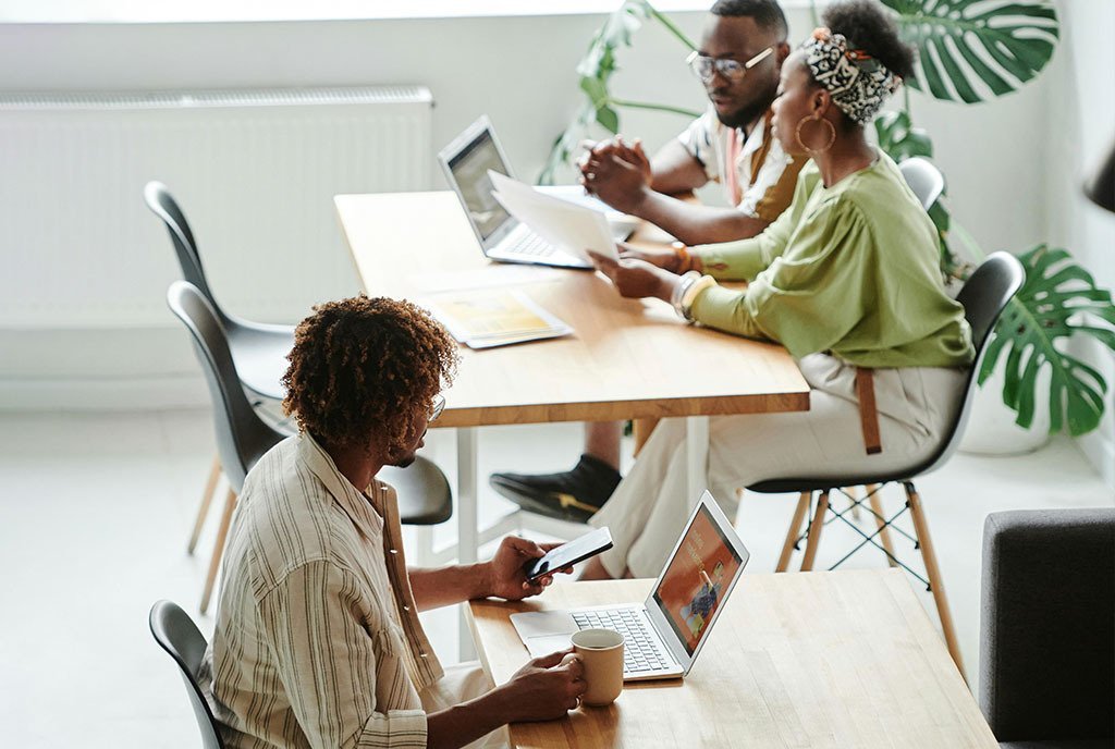 Photo of Black entrepreneurs in a co-working space.  Two are working together, another is doing their own work on the computer with their coffee.
