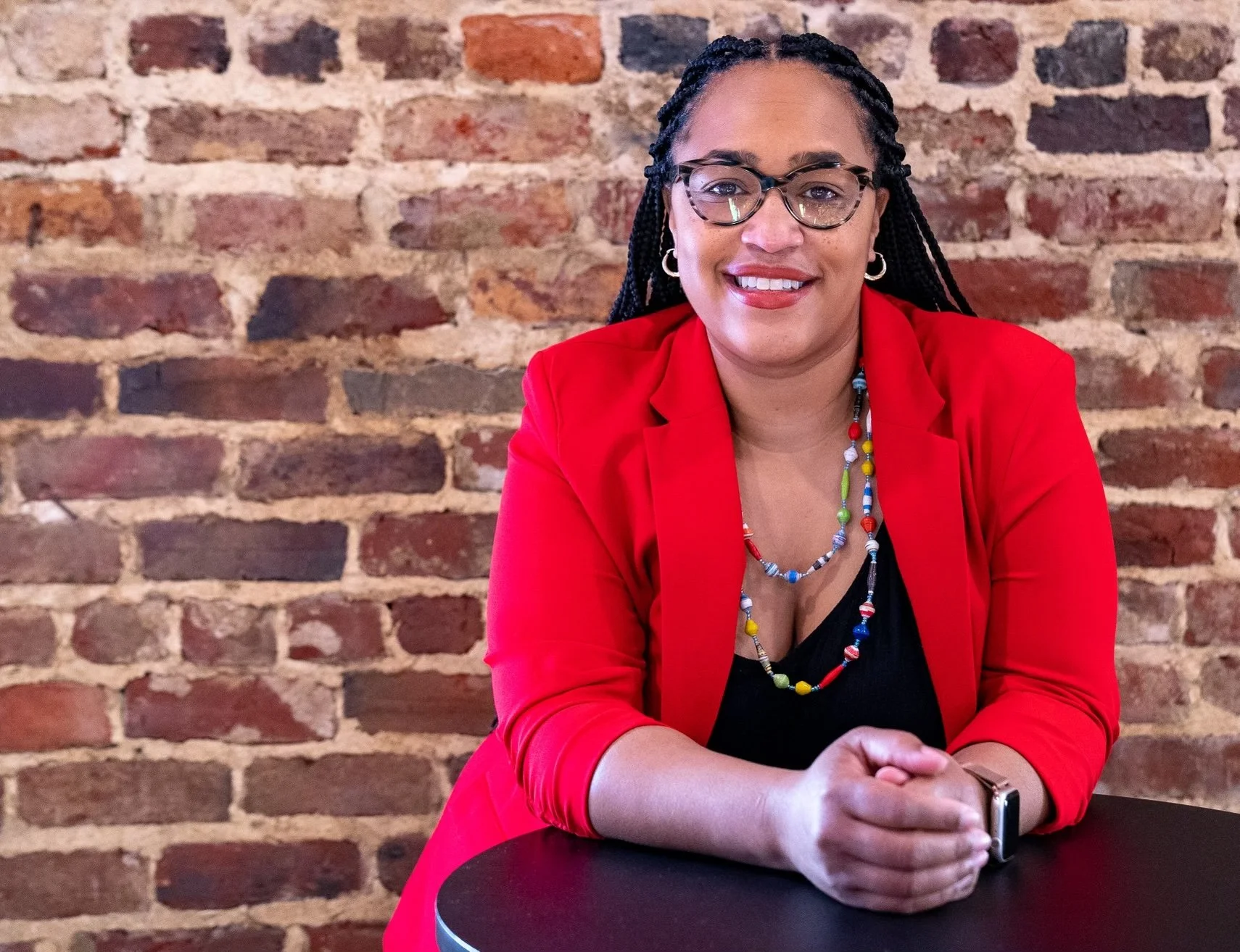 Rasheeda Creighton, Executive Director of BLCK Street, in a red blazer with her hands folded on a table.