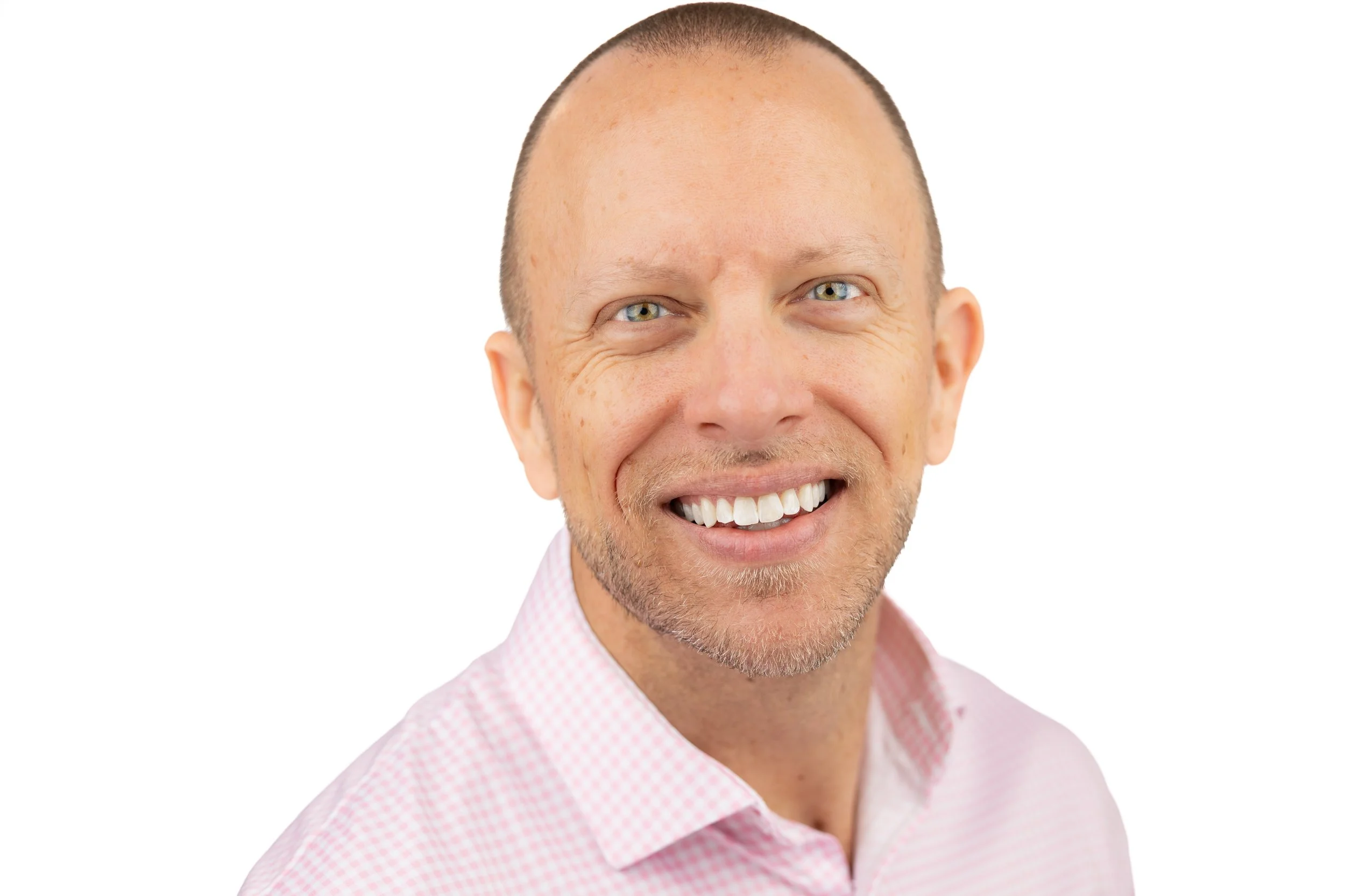 Close-up of a smiling middle-aged man with a light beard and blue eyes, wearing a pink checkered shirt, against a white background.