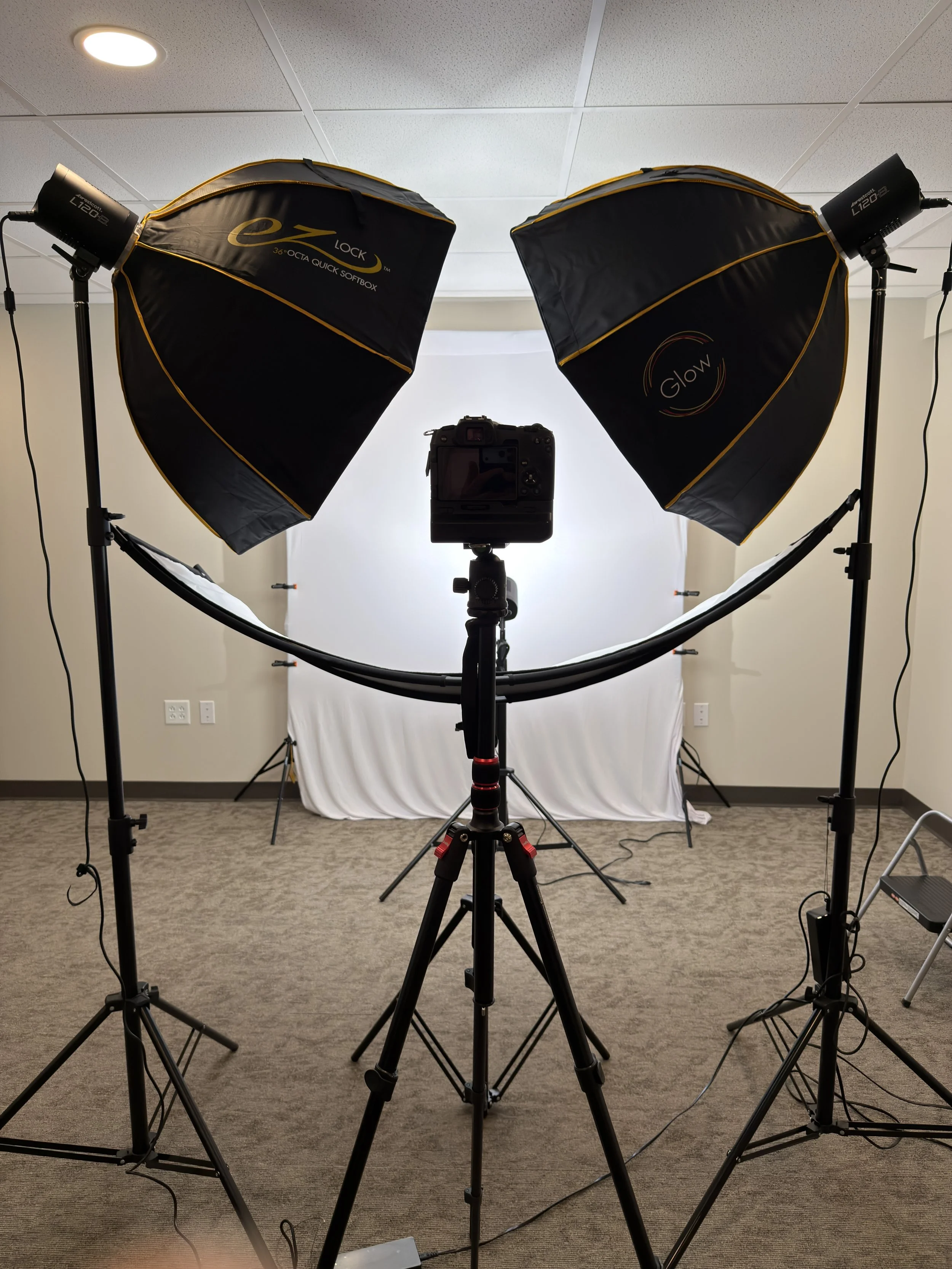 Photography studio setup with two softbox lights, a camera on tripod, and a white backdrop.