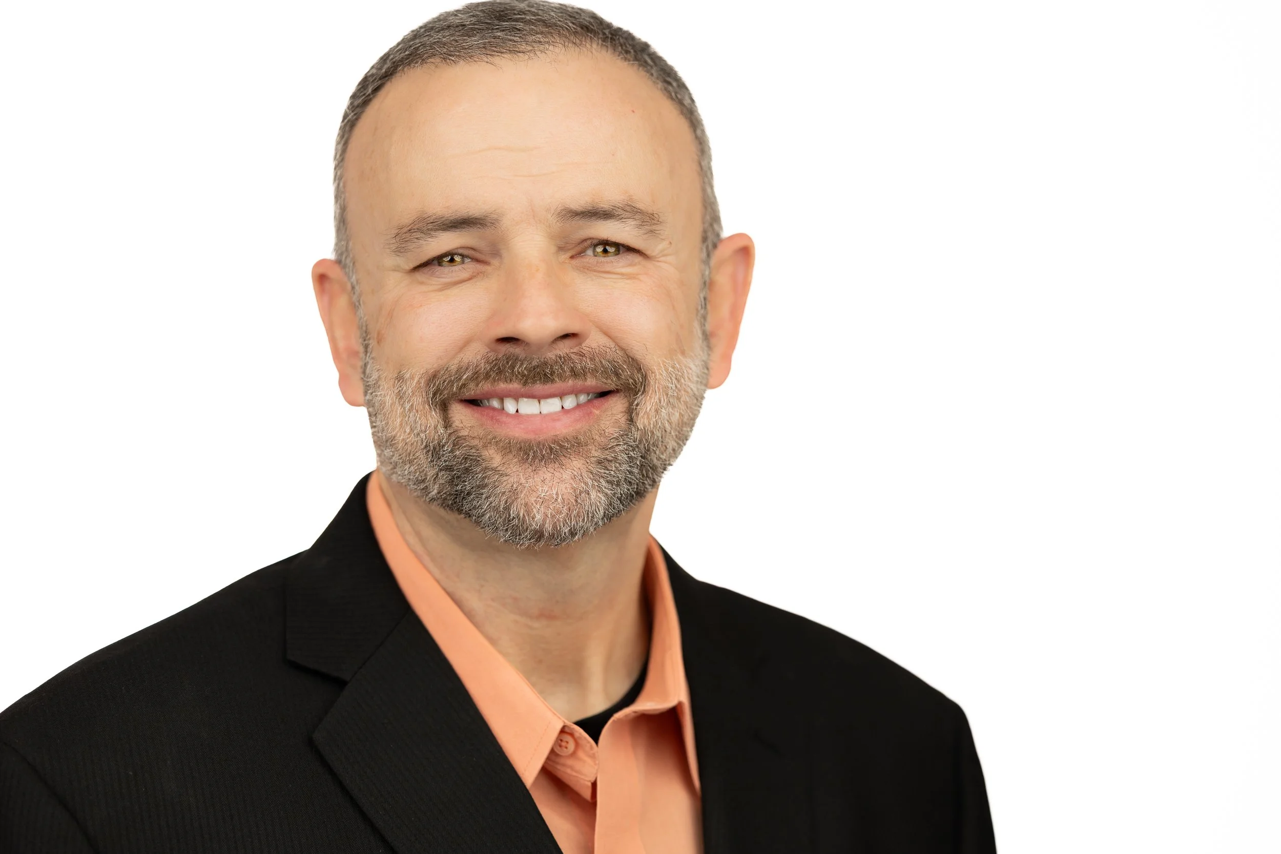 Professional headshot of a middle-aged man with a beard, wearing a black suit jacket and a peach-colored shirt, smiling at the camera against a white background.